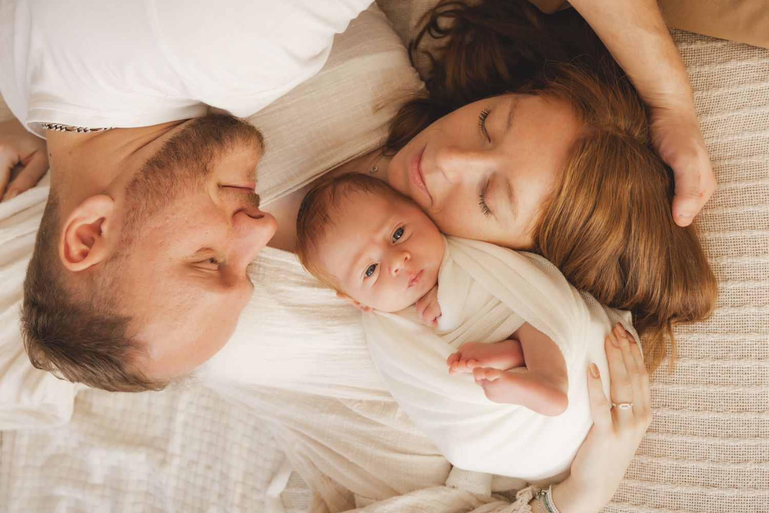 Parents lying together on bed, lovingly cuddling their newborn baby between them.