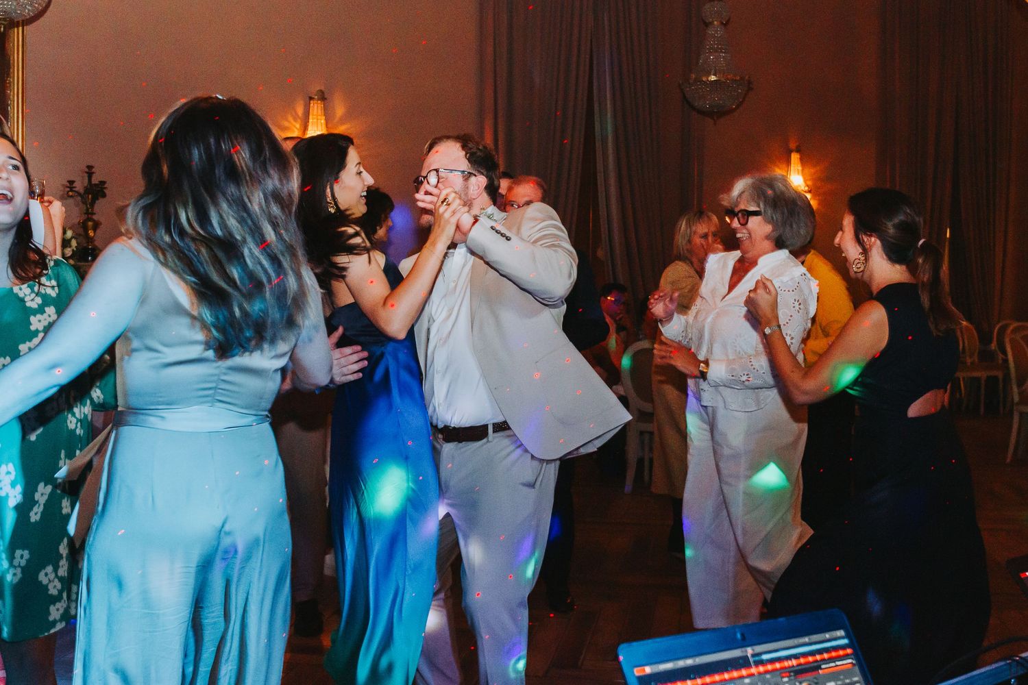 Guests dancing joyfully at an elegant wedding reception with colorful lights on the dance floor.