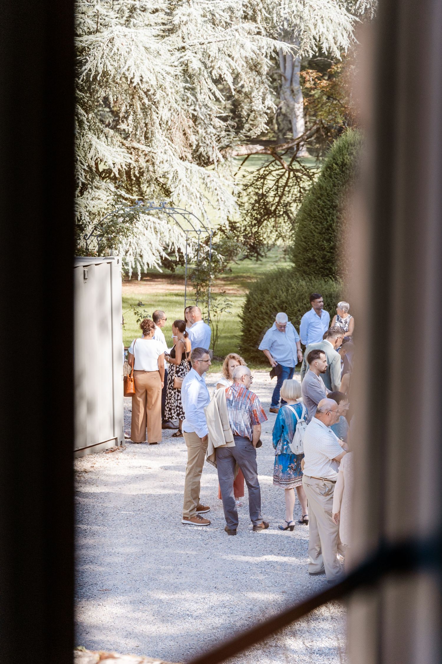 Wedding guests mingling on a gravel path surrounded by lush trees at a French chateau venue.