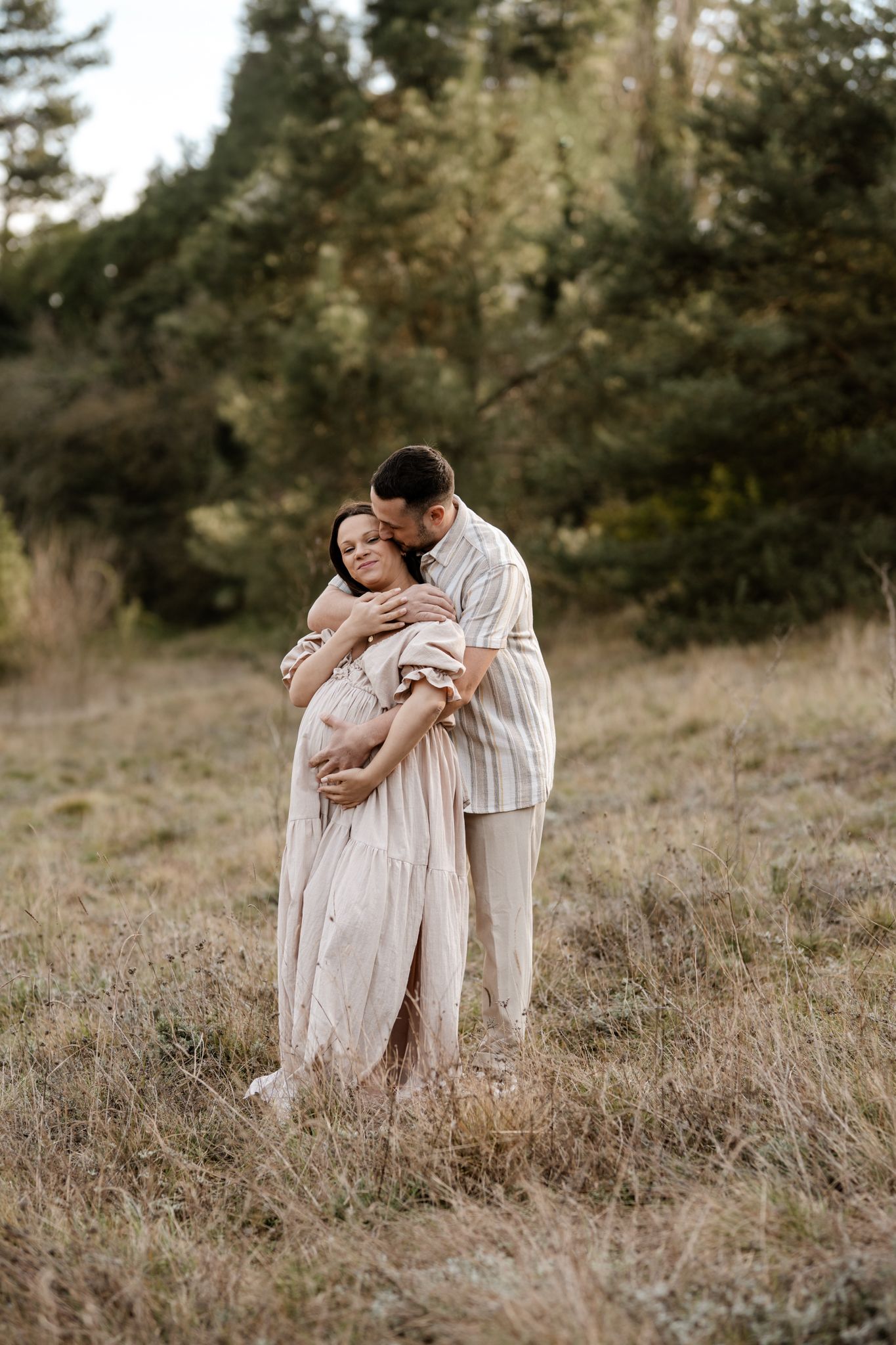 Séance photo couple en Isère : l'étreinte complice et chaleureuse de futurs parents au cœur d'un champ en pleine nature.
