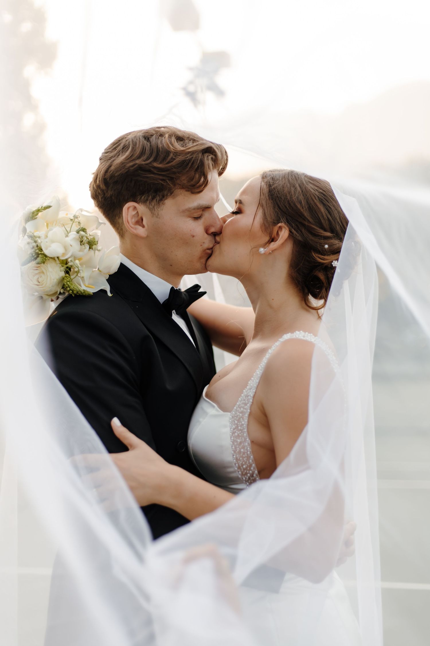 Elegant wedding couple shares romantic kisses under flowing white veil.
