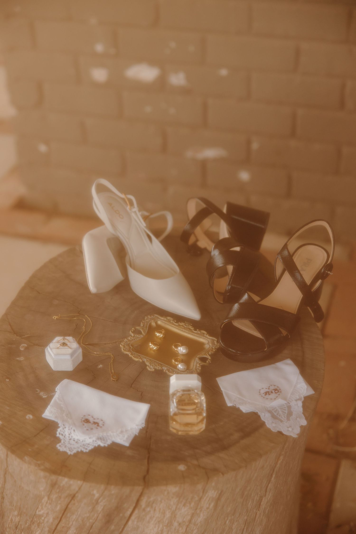 Wedding accessories including white and black shoes, jewelry, and delicate lace details arranged on wooden table.