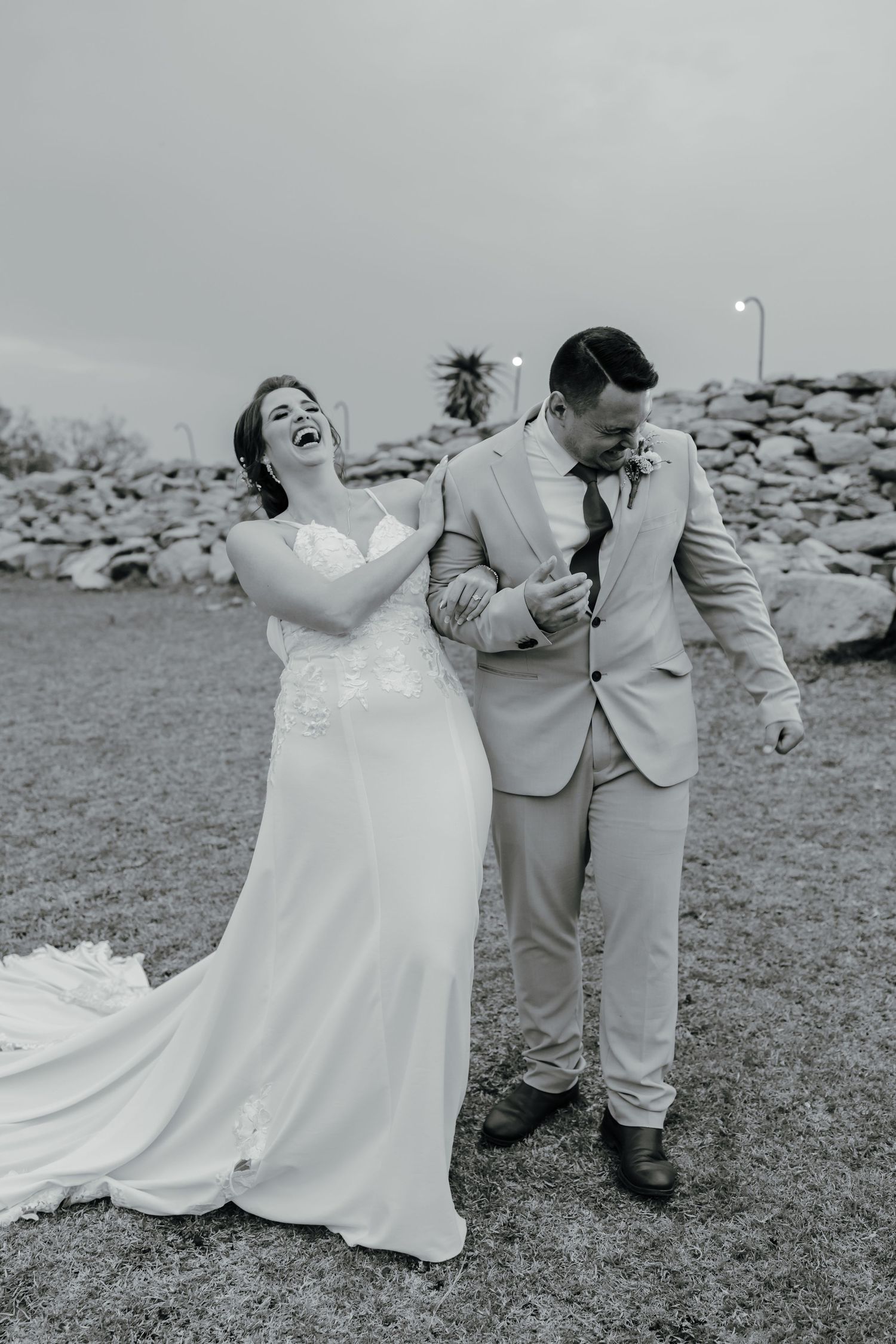 A black and white candid wedding photo showing a couple sharing a laugh outdoors.