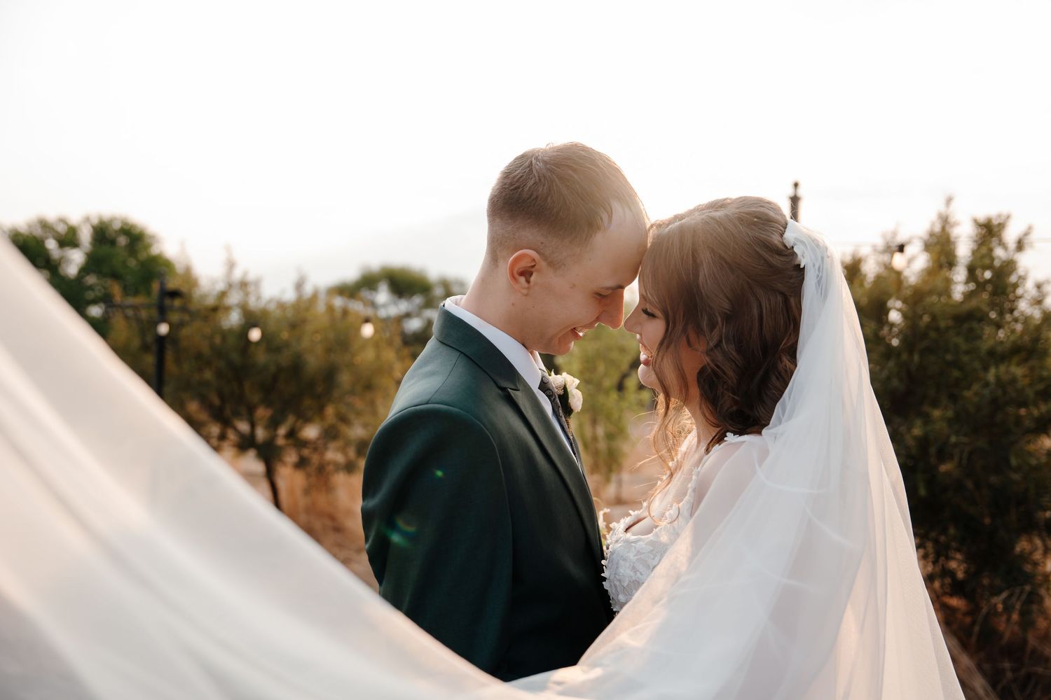 Romantic wedding couple embraces against flowing white veil backdrop.
