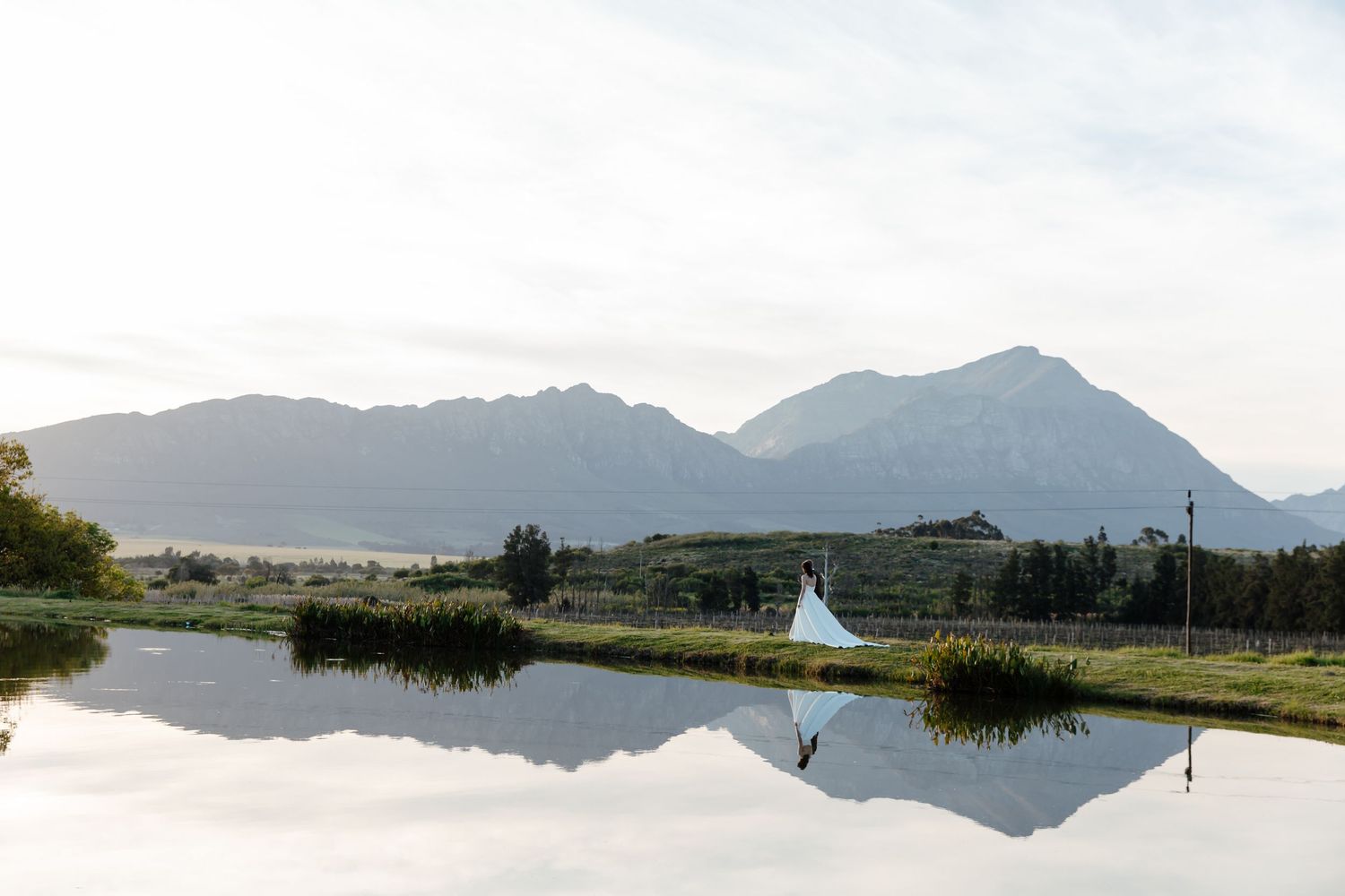 A serene lake reflects mountains and a small white teepee structure against a cloudy sky in a peaceful landscape.