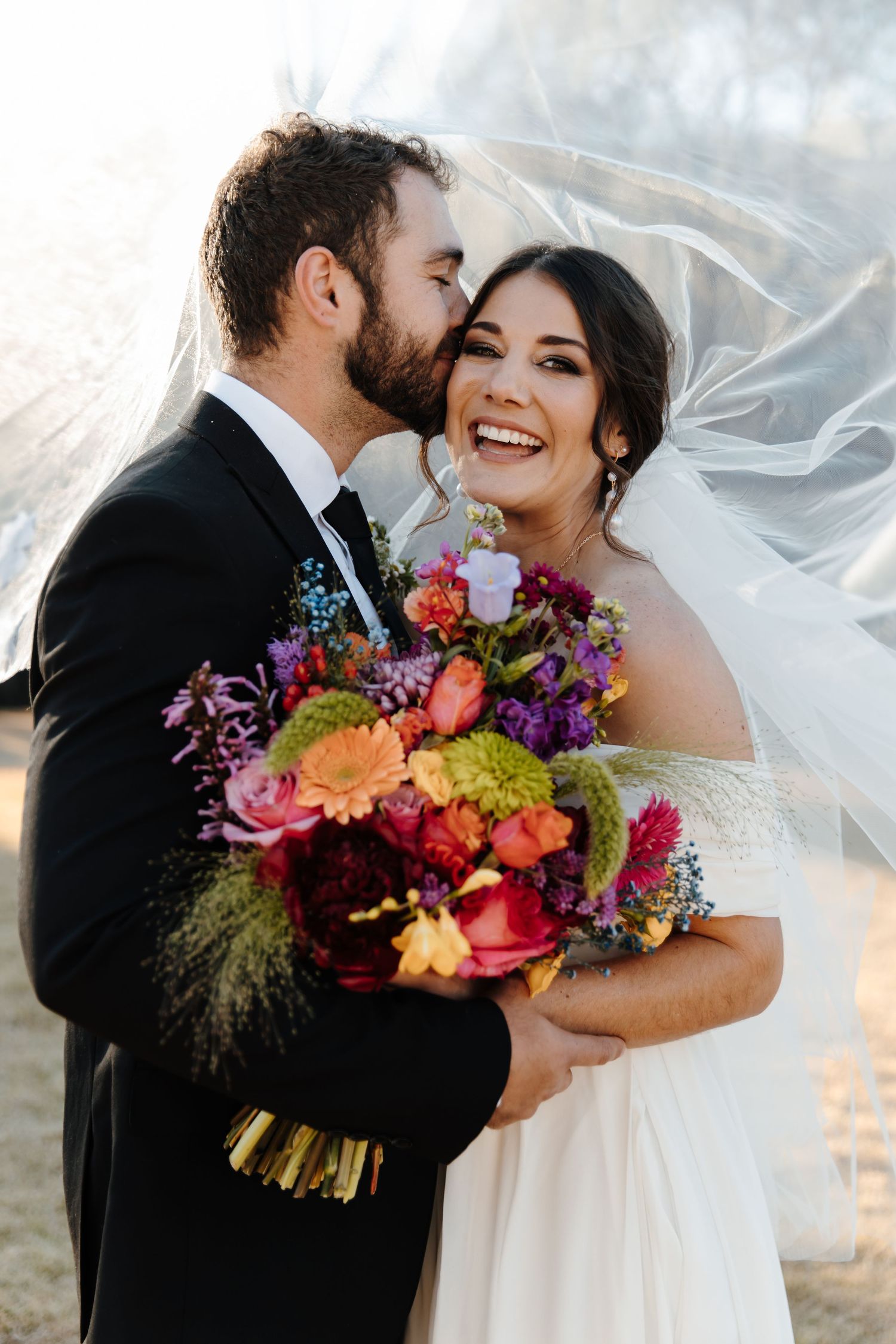 Romantic wedding couple shares a joyful moment with vibrant colorful bouquet at sunset.