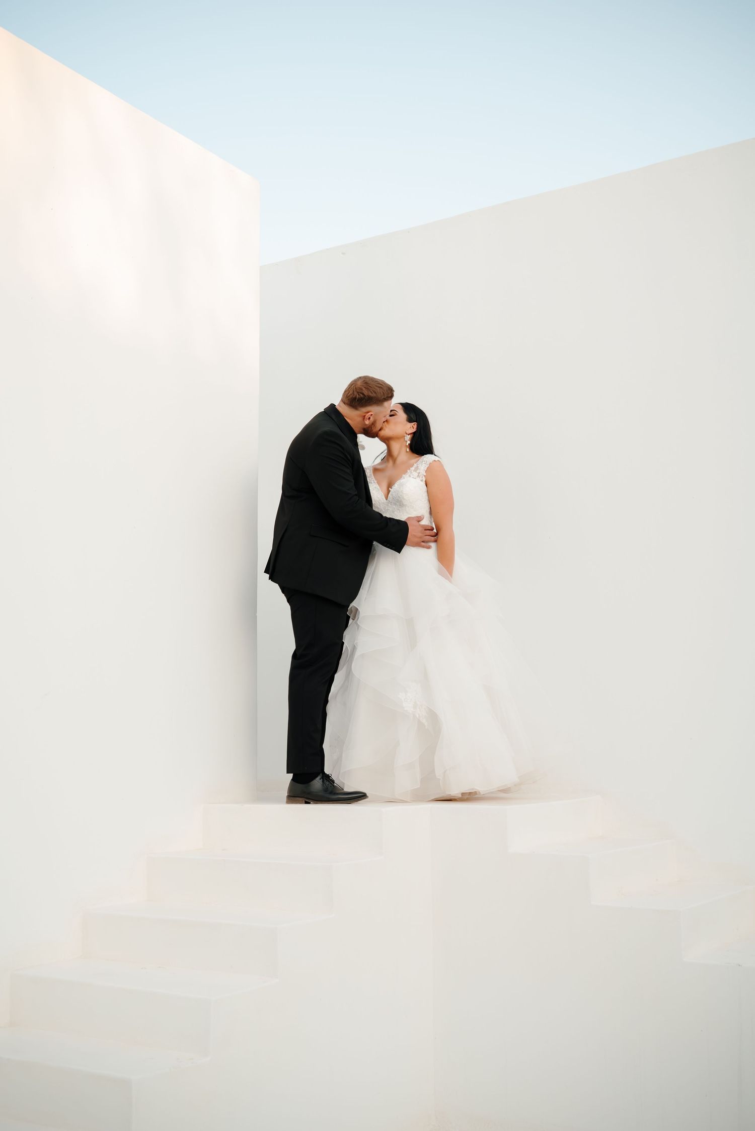 A bride and groom share an intimate dip pose in a minimalist white studio setting for their wedding portraits.