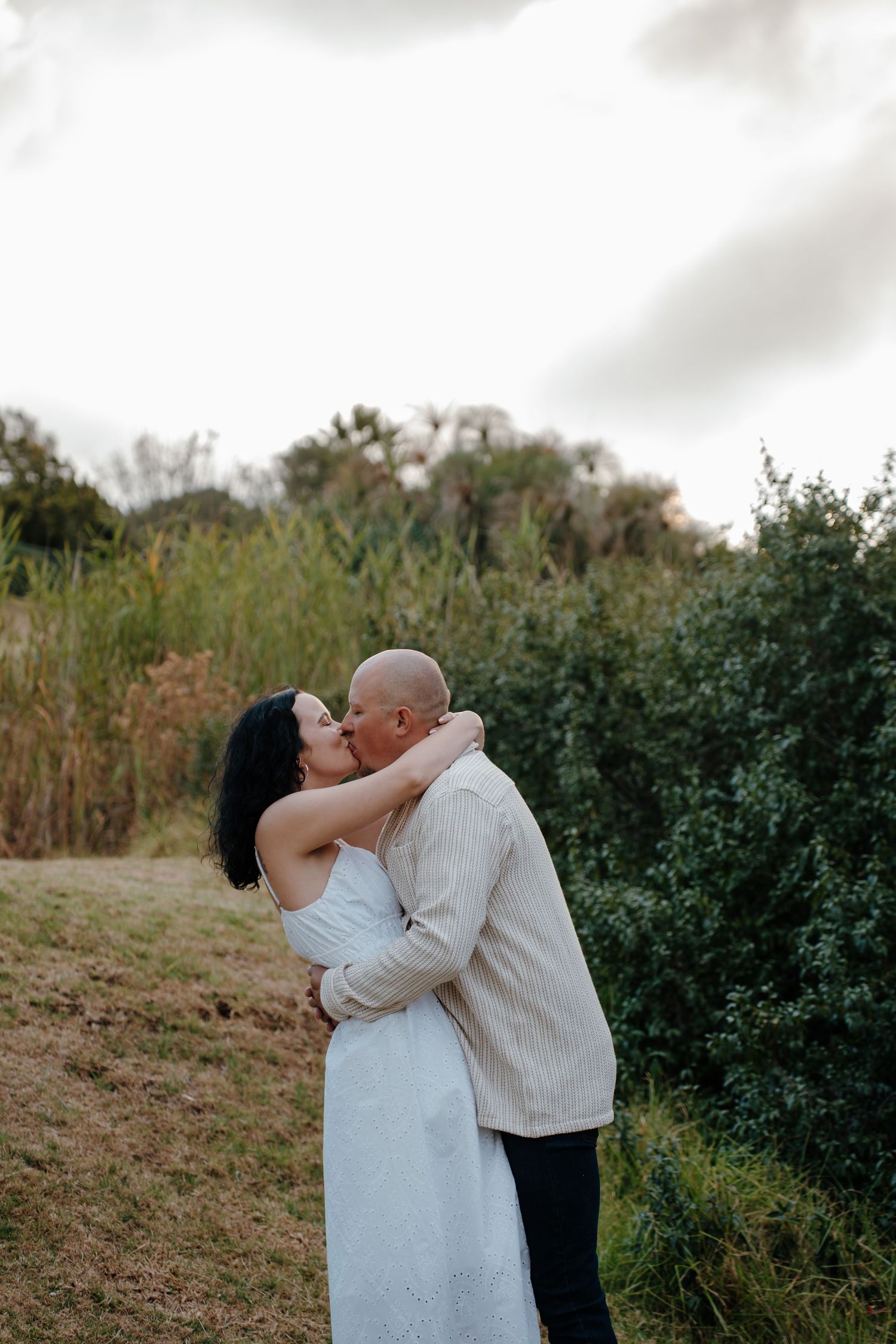 Couple in wedding attire embraces tenderly in a natural outdoor setting.