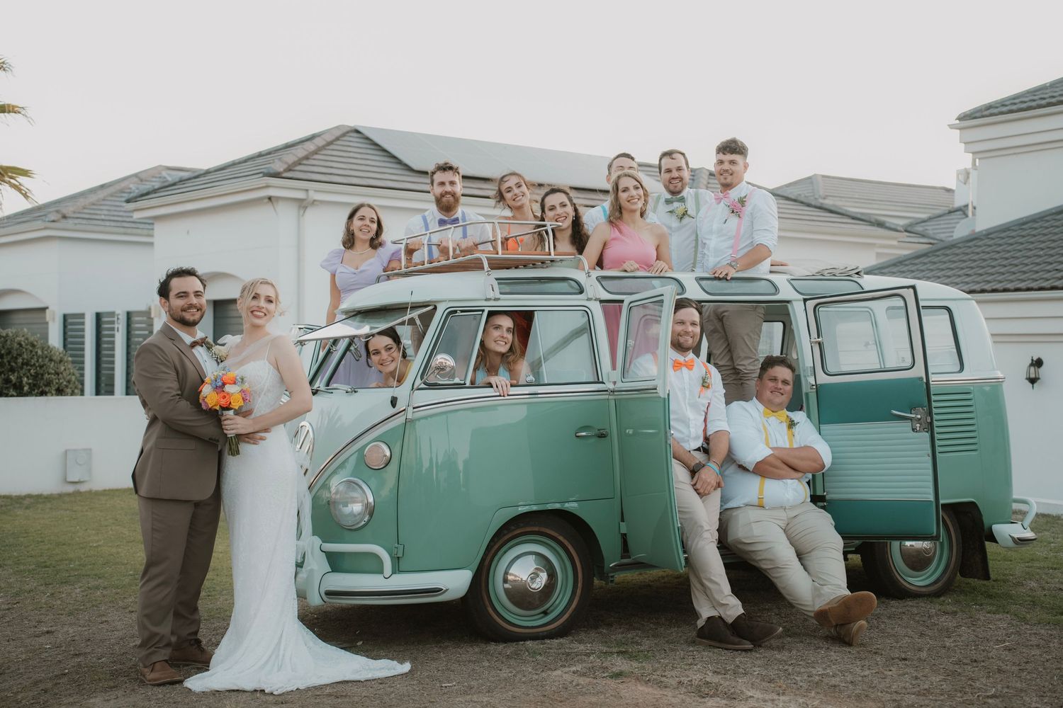 Wedding party poses with vintage mint green Volkswagen van in casual group photo.