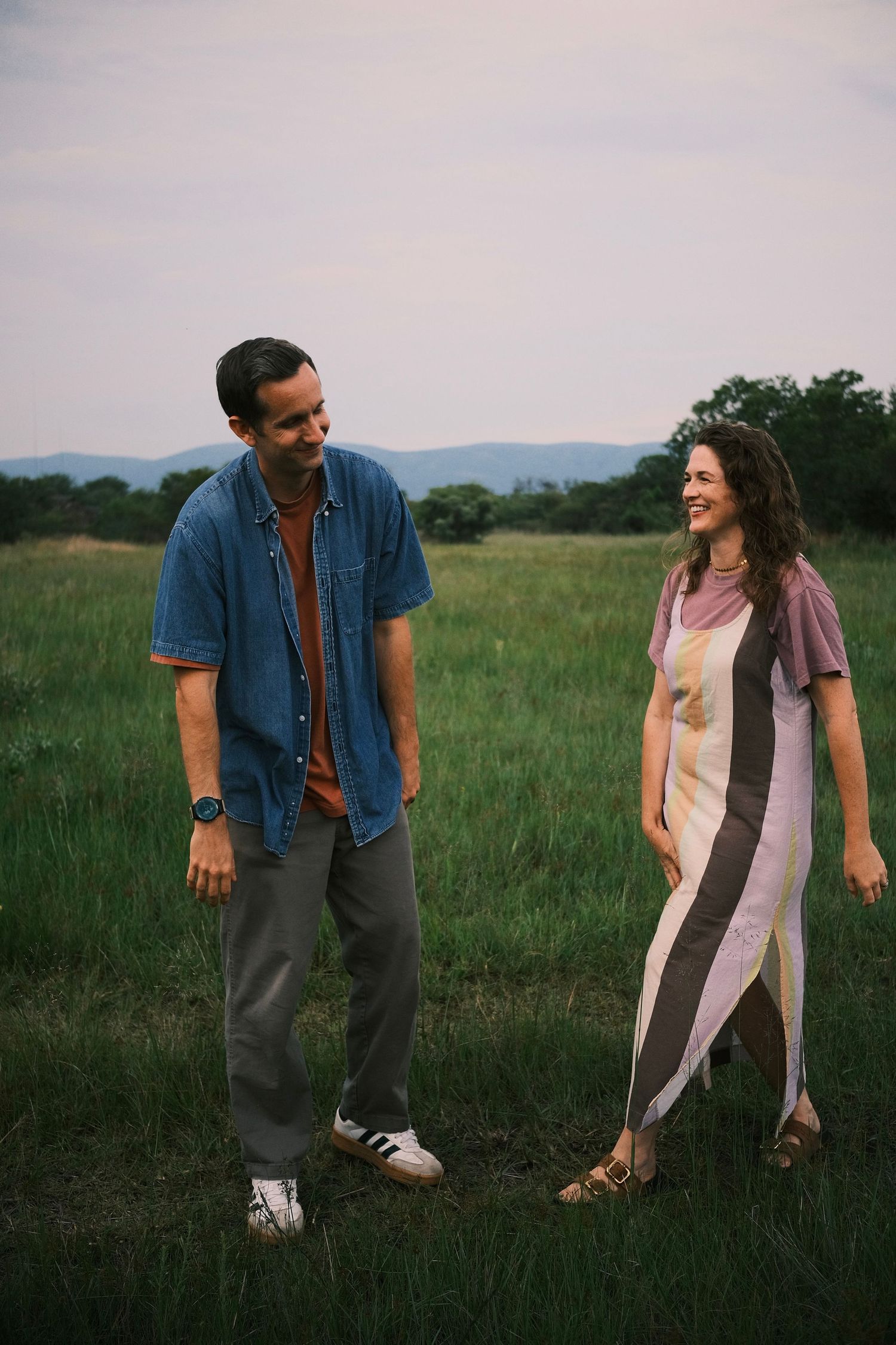 A smiling couple walks together in a lush green field at dusk.