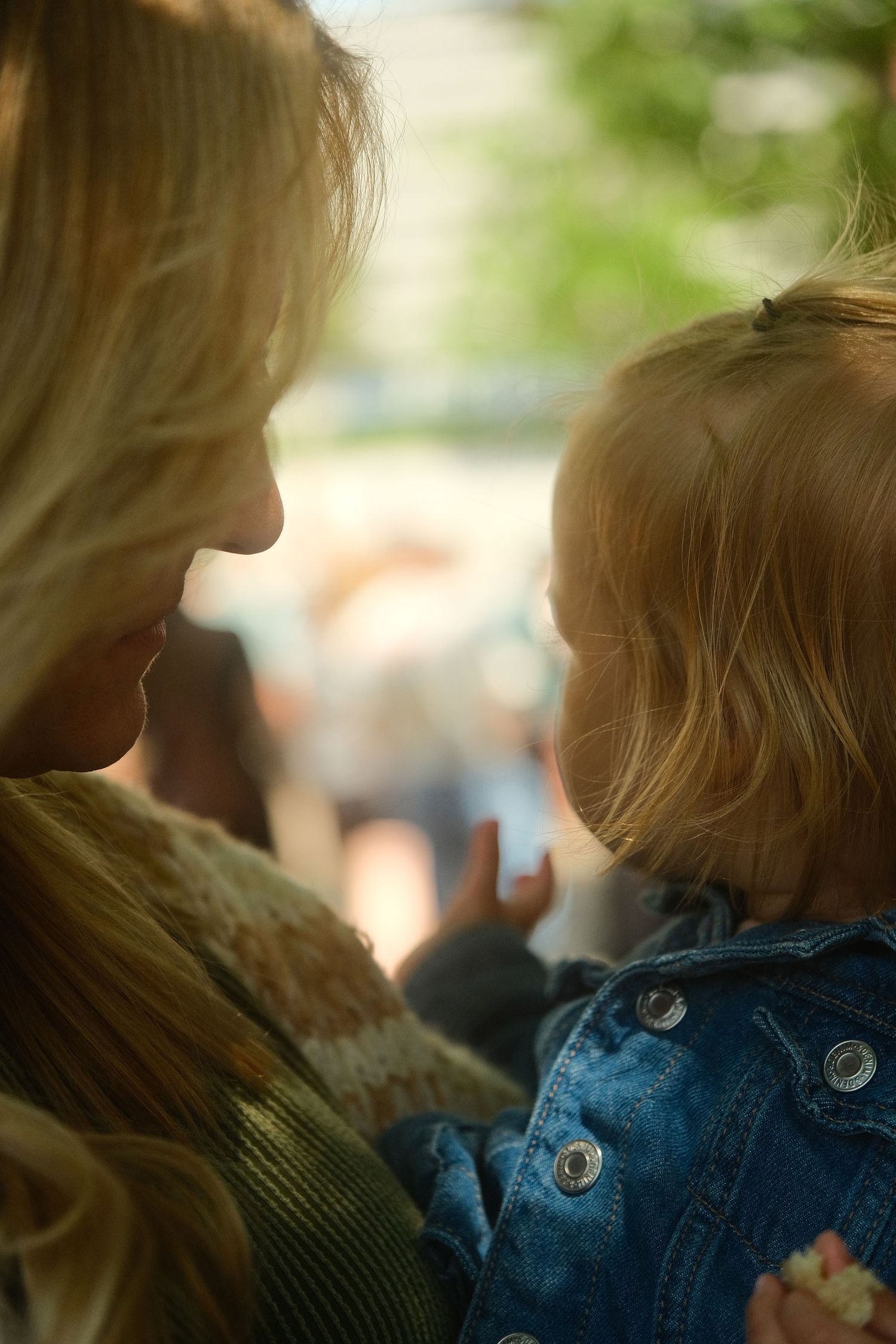 Mother tenderly holding and gazing at her young toddler outdoors in soft light.