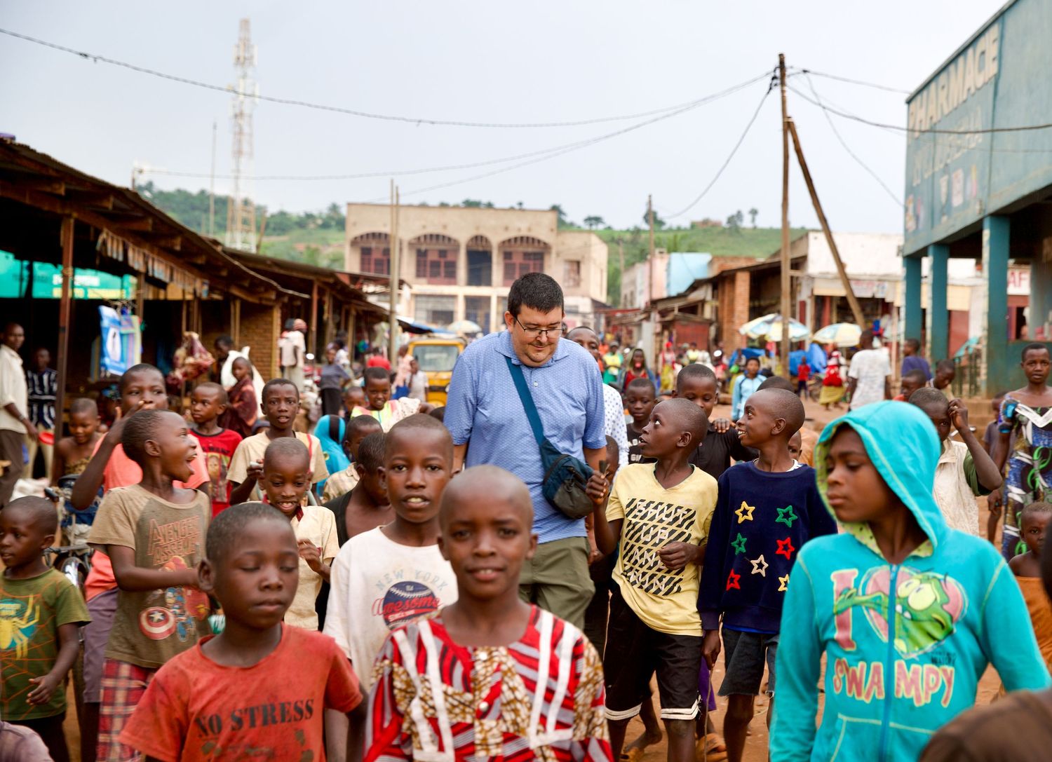 Western man walking through busy African market street surrounded by large group of local children.