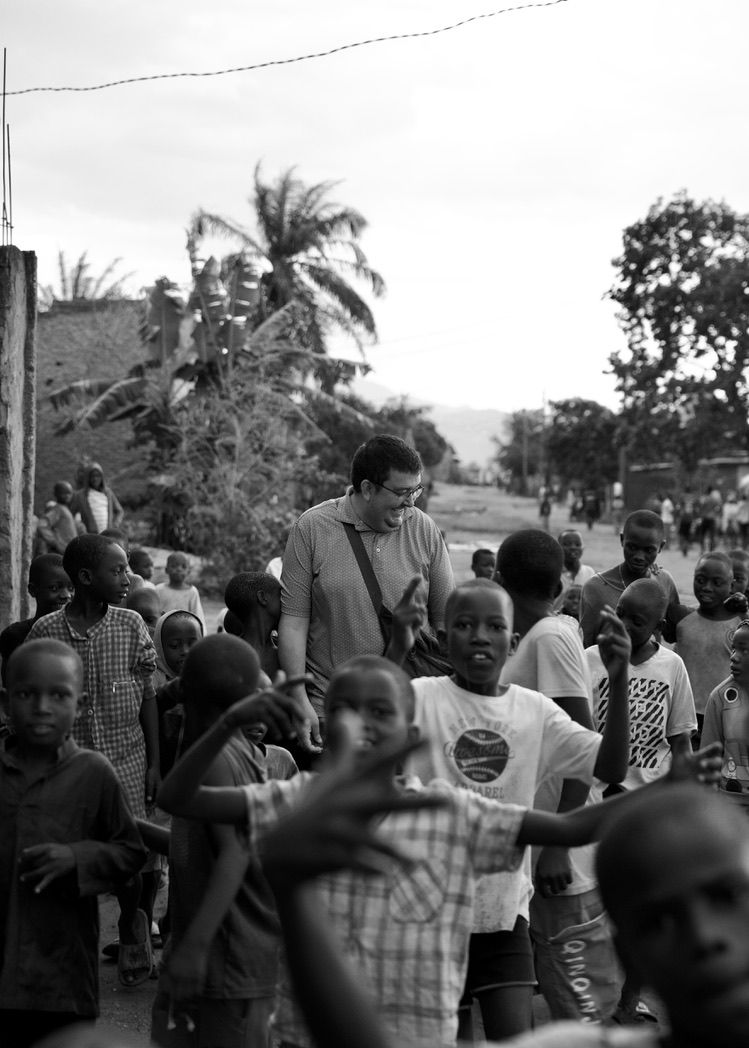 A man walks among a large group of African children on a dirt road.