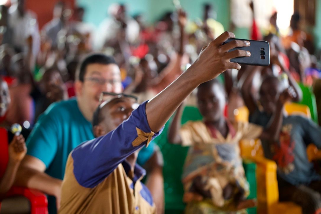 African woman taking a selfie with a smiling Asian man at a lively community gathering event indoors.