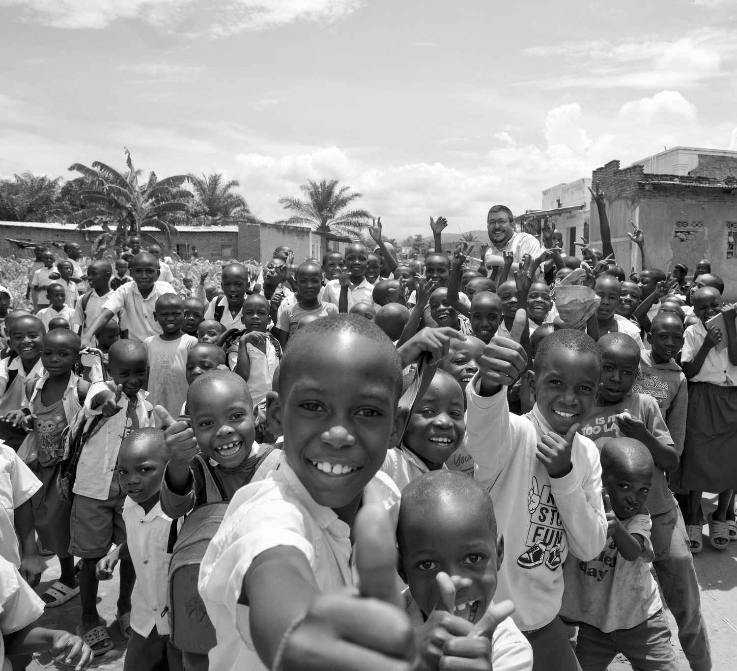 Large group of joyful African children waving and smiling at camera outdoors.