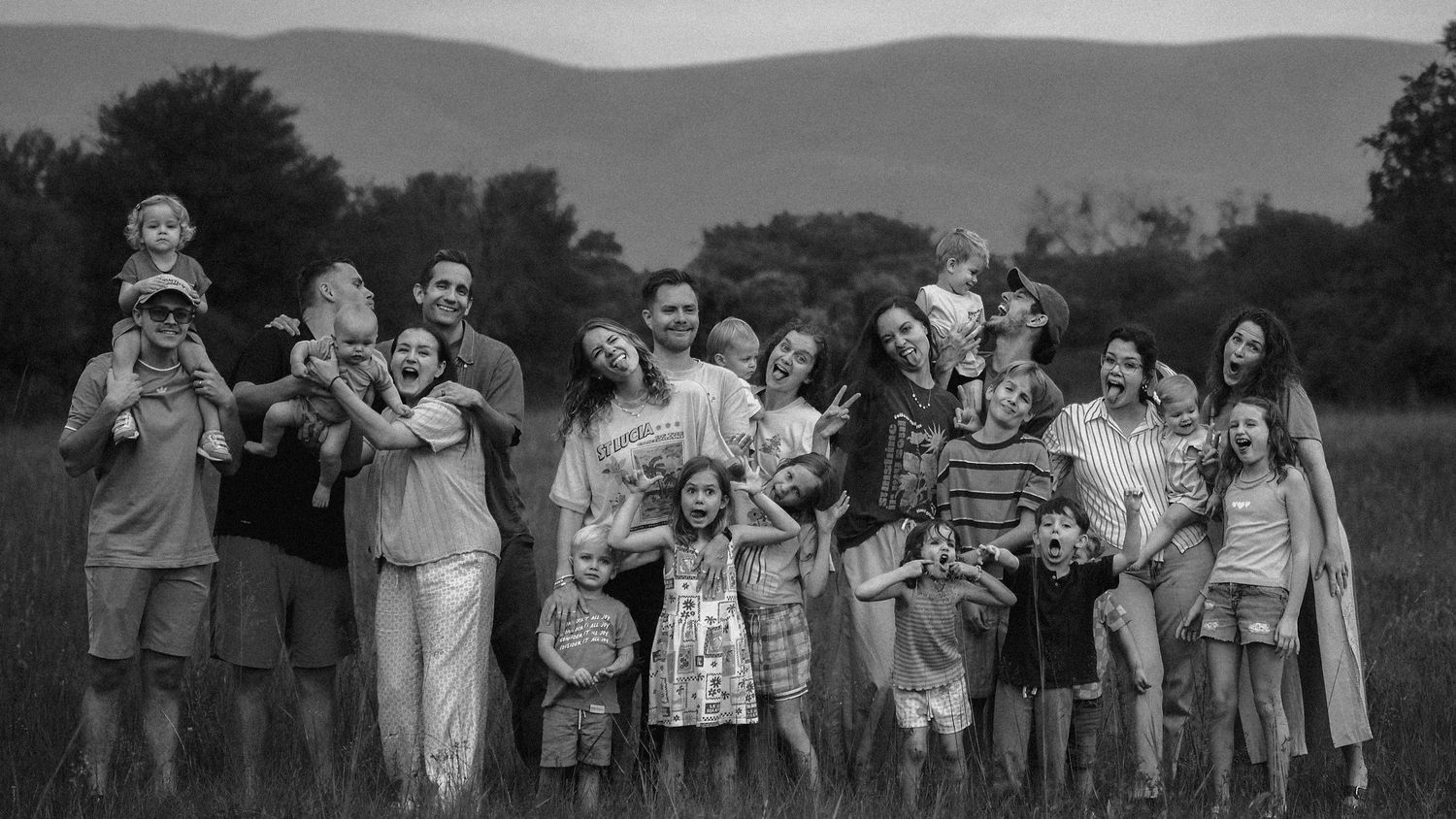 A joyful multigenerational family gathers for a group portrait in a green field.