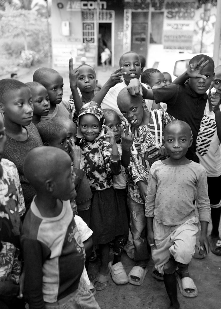 A large group of African children gather on a street, smiling and gesturing at the camera.