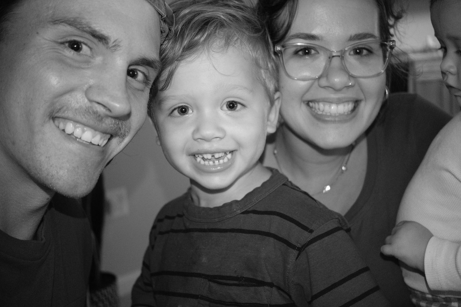 Black and white photo of two parents and a toddler smiling together.