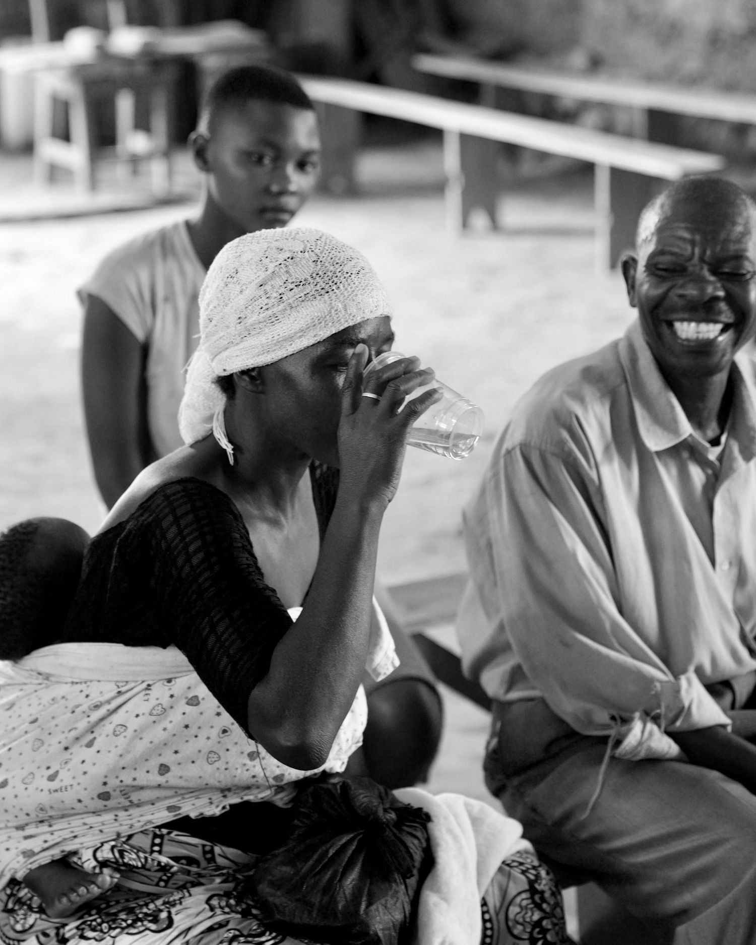 Black and white portrait of an emotional African woman wiping tears beside a laughing elderly man outdoors.