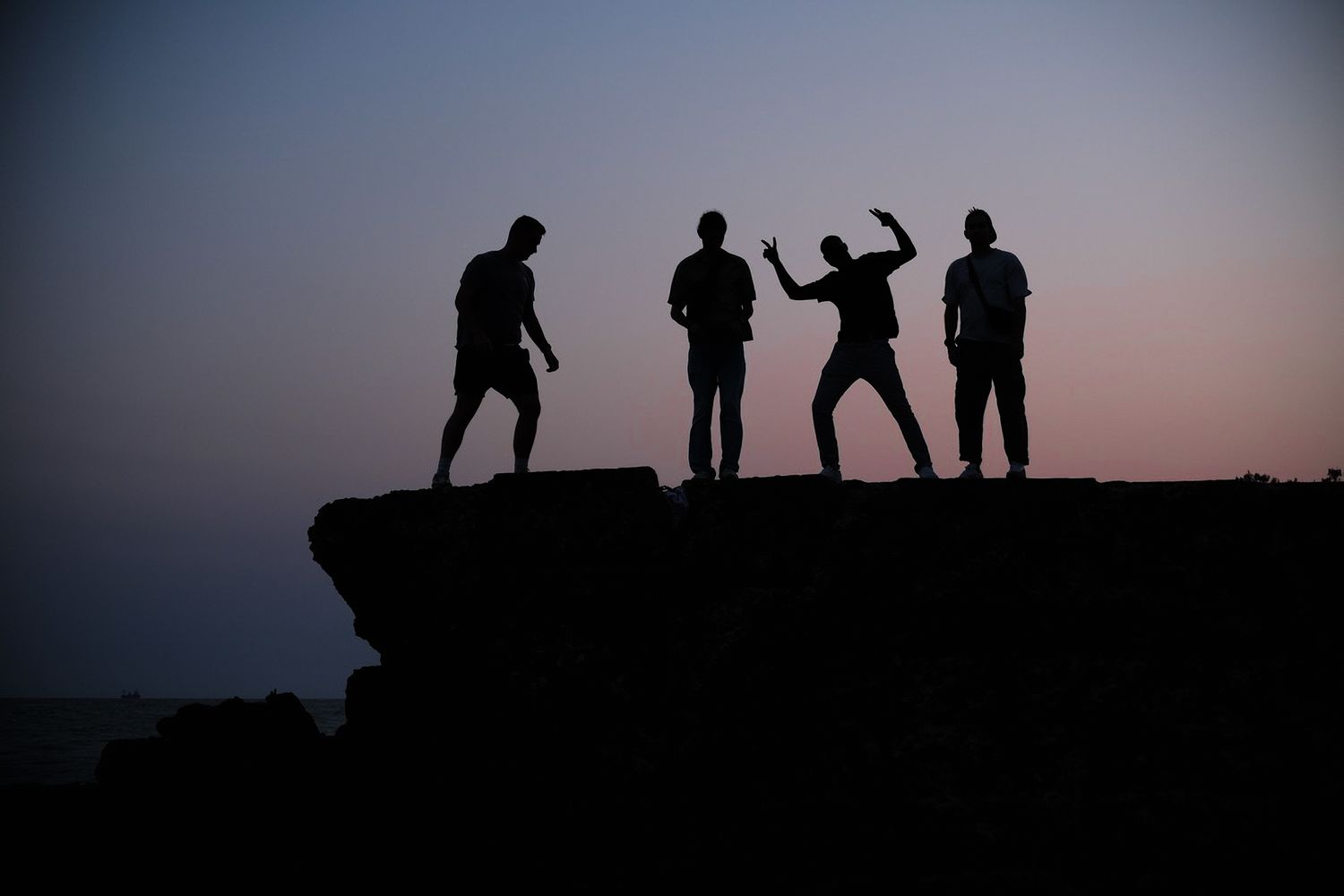 Silhouettes of four people posing on a rocky cliff at dusk.