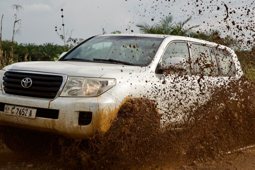 White Toyota Land Cruiser splashing through muddy water on an off-road dirt track.