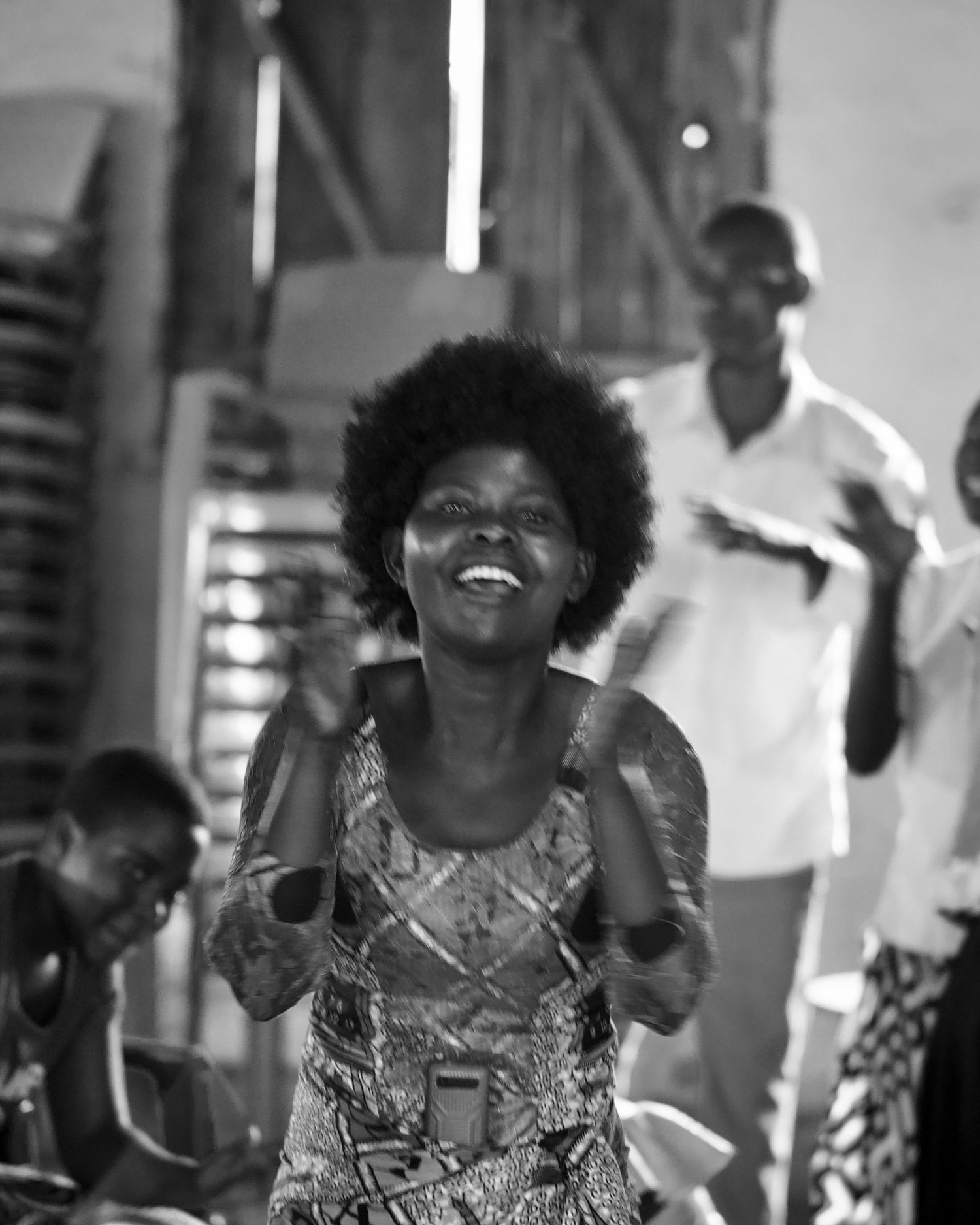Joyful African woman with afro hair laughing and dancing in a black and white candid photo.