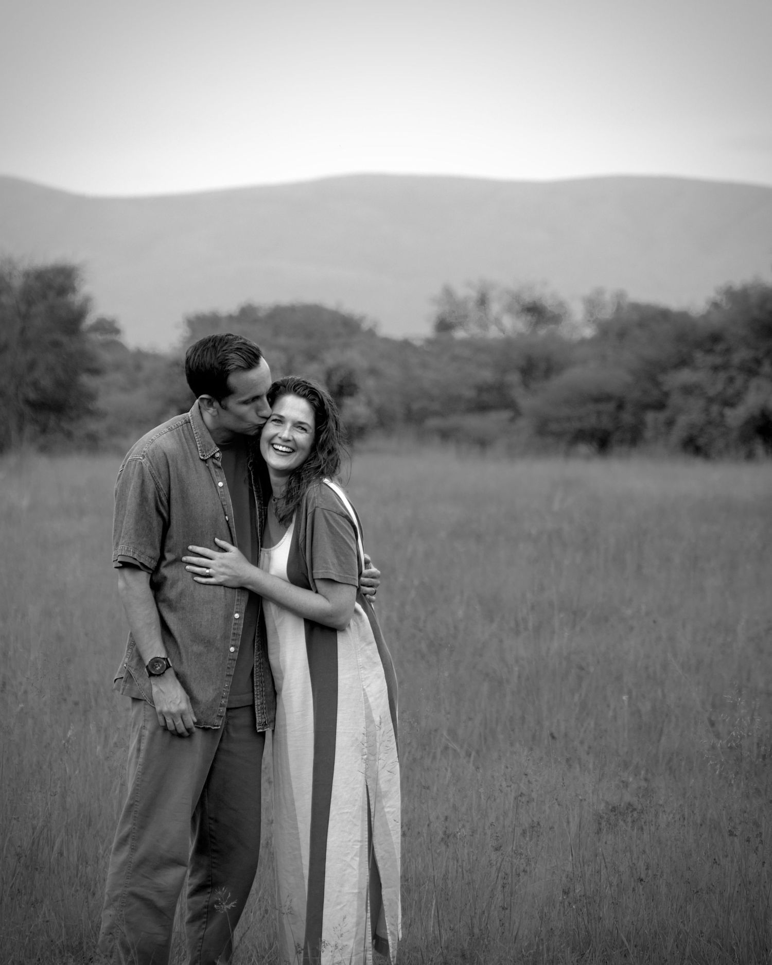 A man tenderly kisses a laughing woman in a striped dress in a meadow.