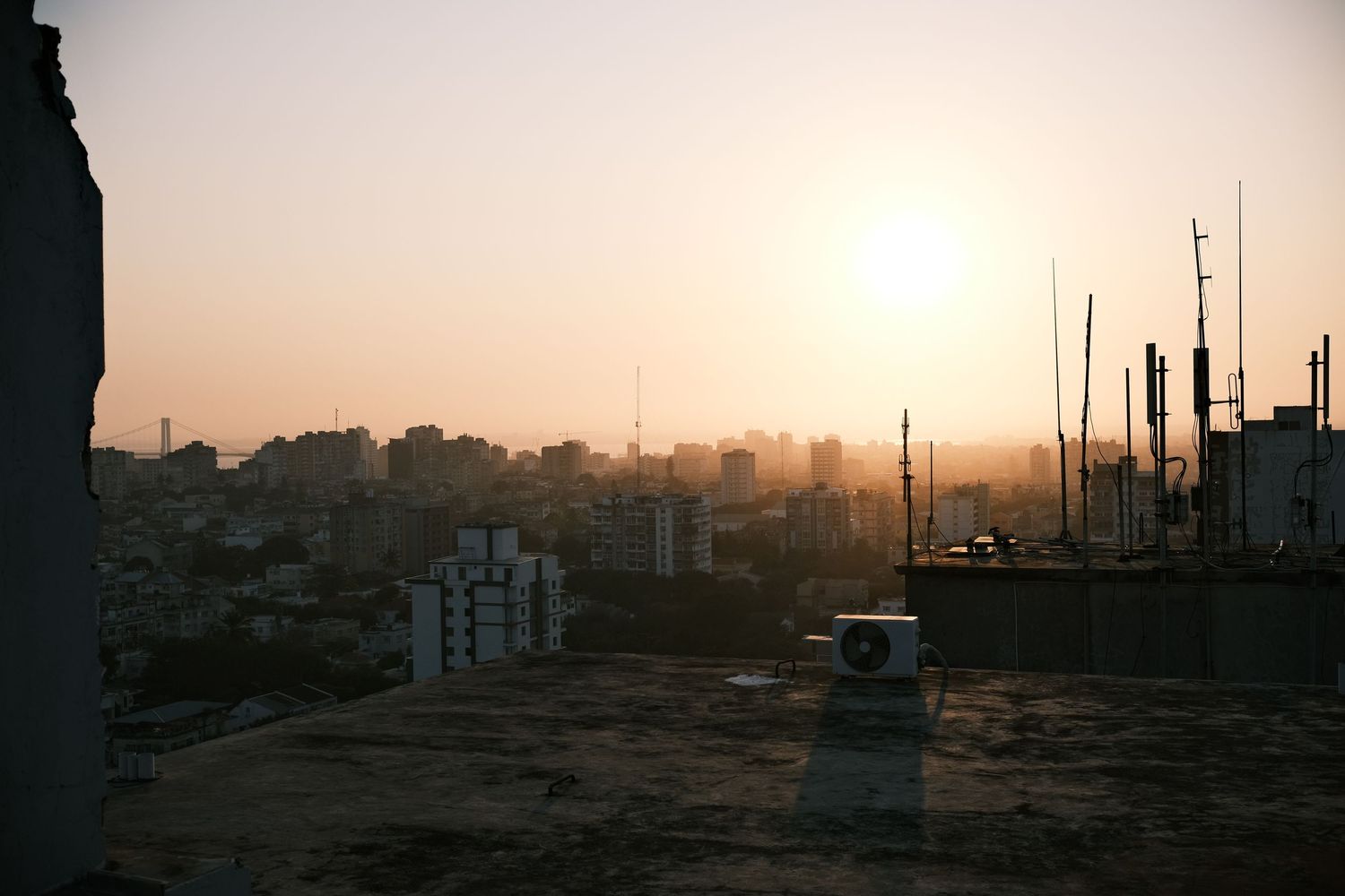Hazy urban skyline at sunset viewed from a rooftop with antennas.
