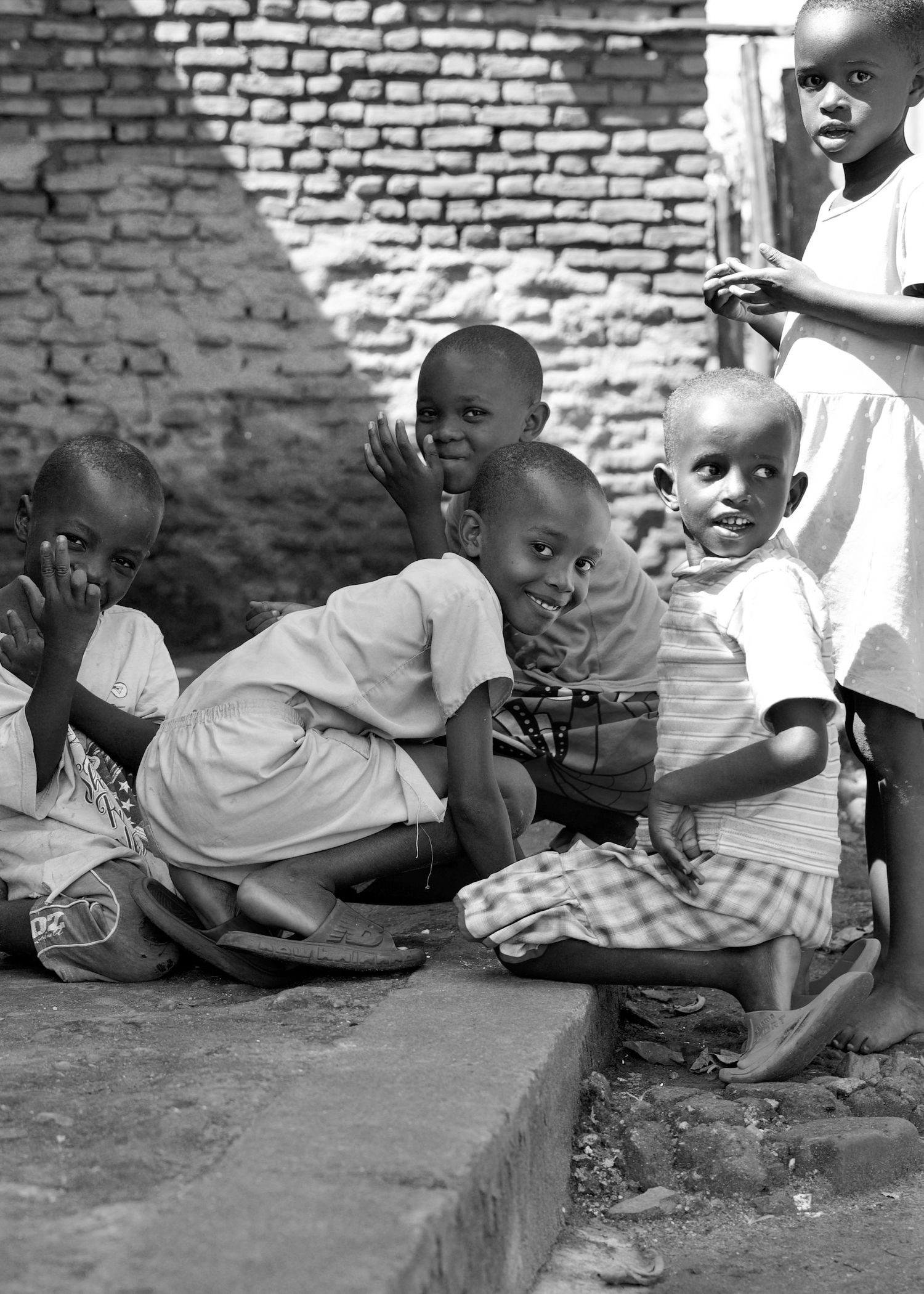 Group of young African children sitting on steps smiling at camera near brick wall.