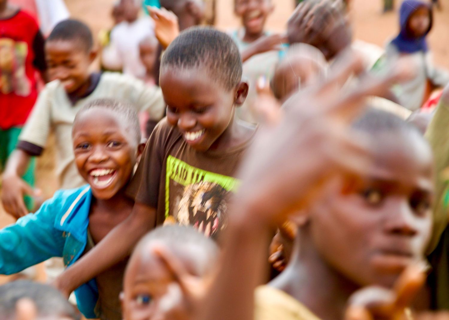 Group of happy African children smiling and waving in an outdoor setting.