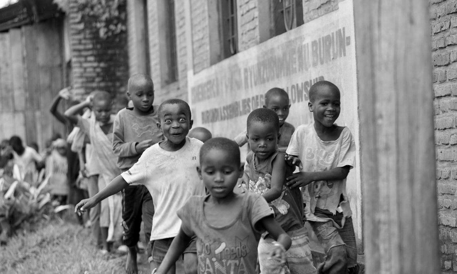 Black and white image of African children laughing and playing outside along a painted wall in Uganda.