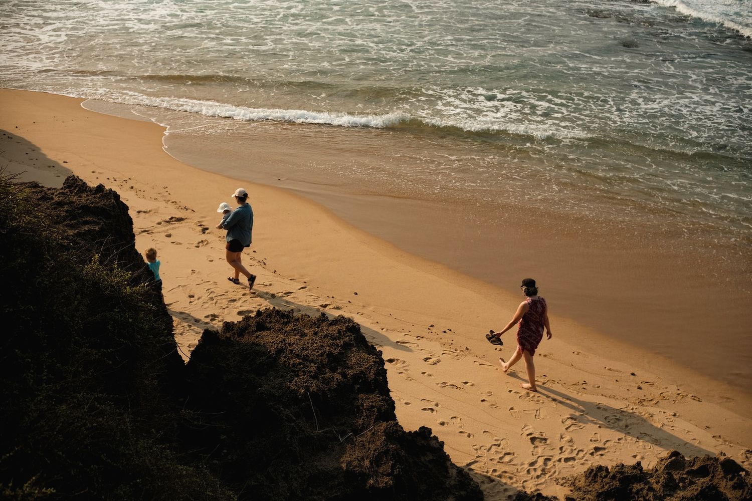 Two people walking along a sandy beach with ocean waves nearby.