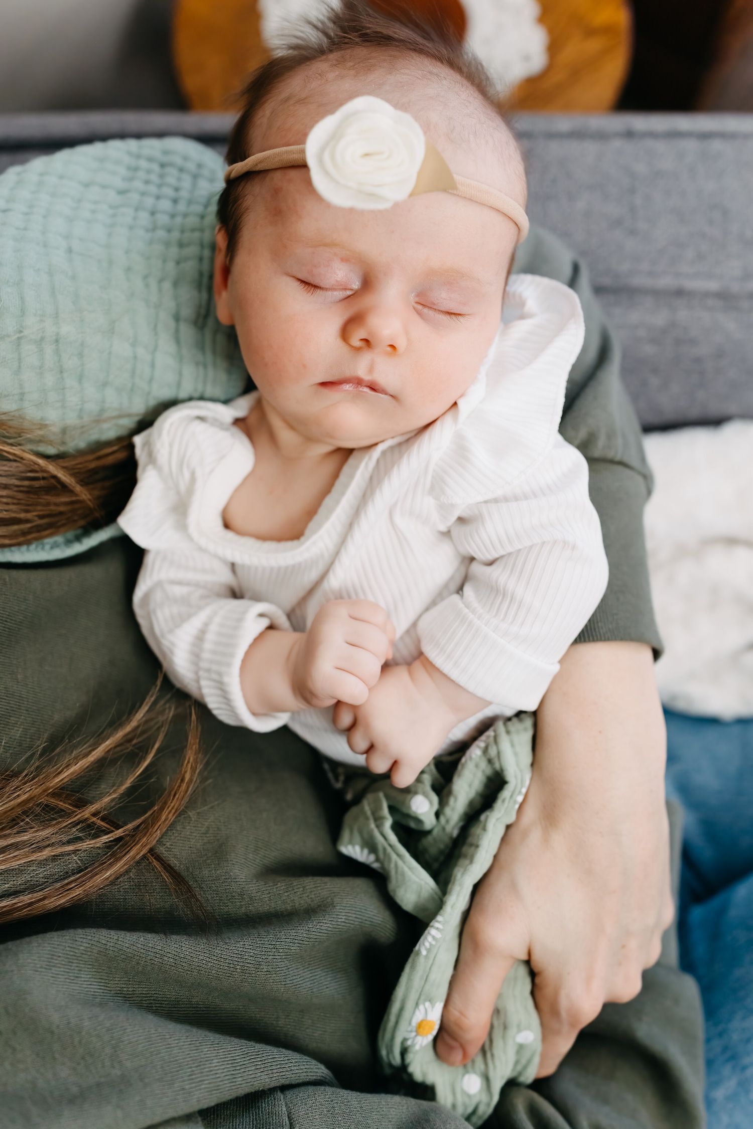 Sleeping baby wearing white knit sweater and mint headband rests peacefully on grey and sage green blankets.