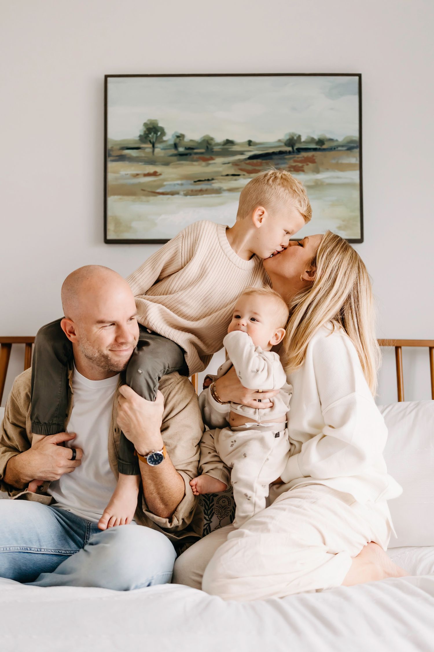 A loving family shares tender moments together while relaxing on a couch beneath landscape artwork.