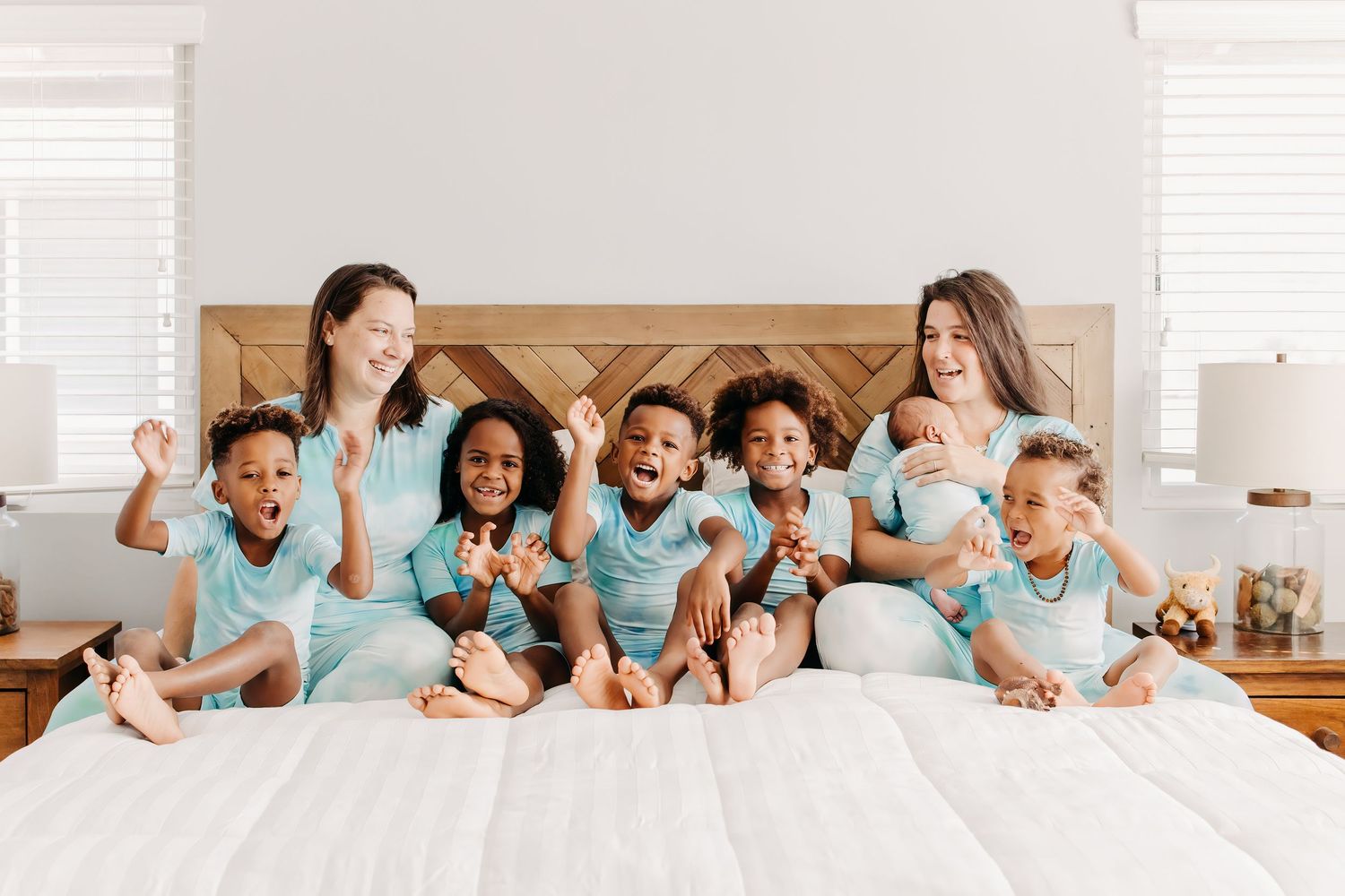 same sex couple wearing matching mint colored outfits lying on bed with their children during an in home newborn session.