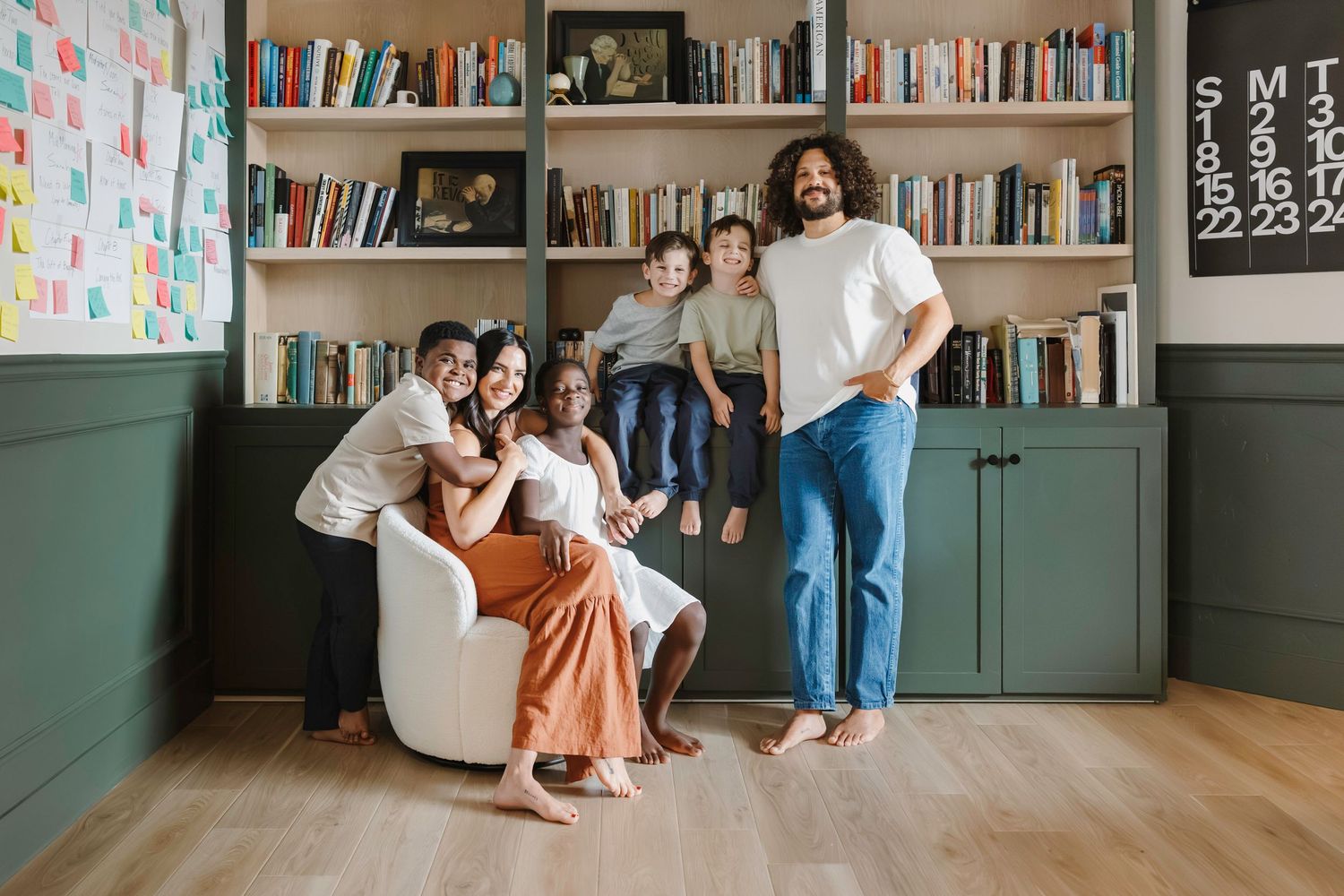 a family of two parents and four children sit in front of a green built in bookshelf