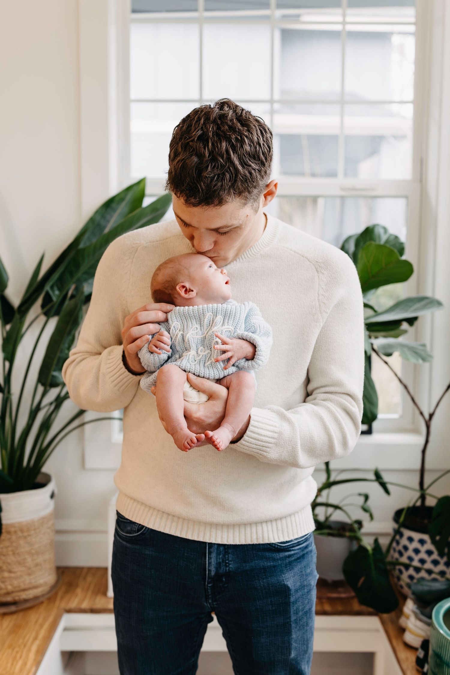 Person in cream sweater holding and lovingly gazing at a small baby in gray knitwear.