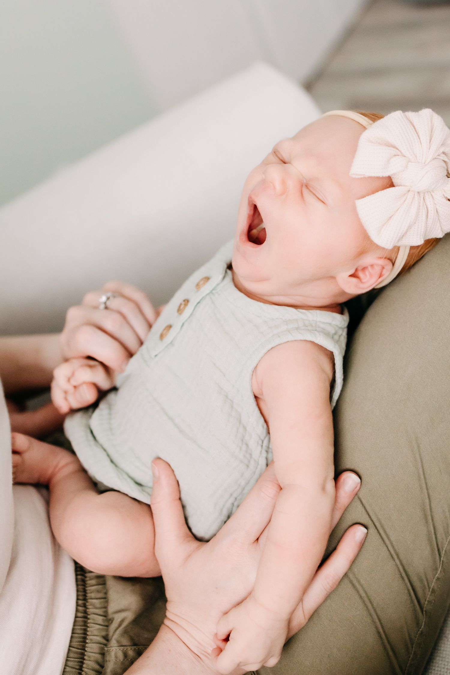 A sleeping baby wearing a light green onesie rests peacefully on a beige couch cushion.