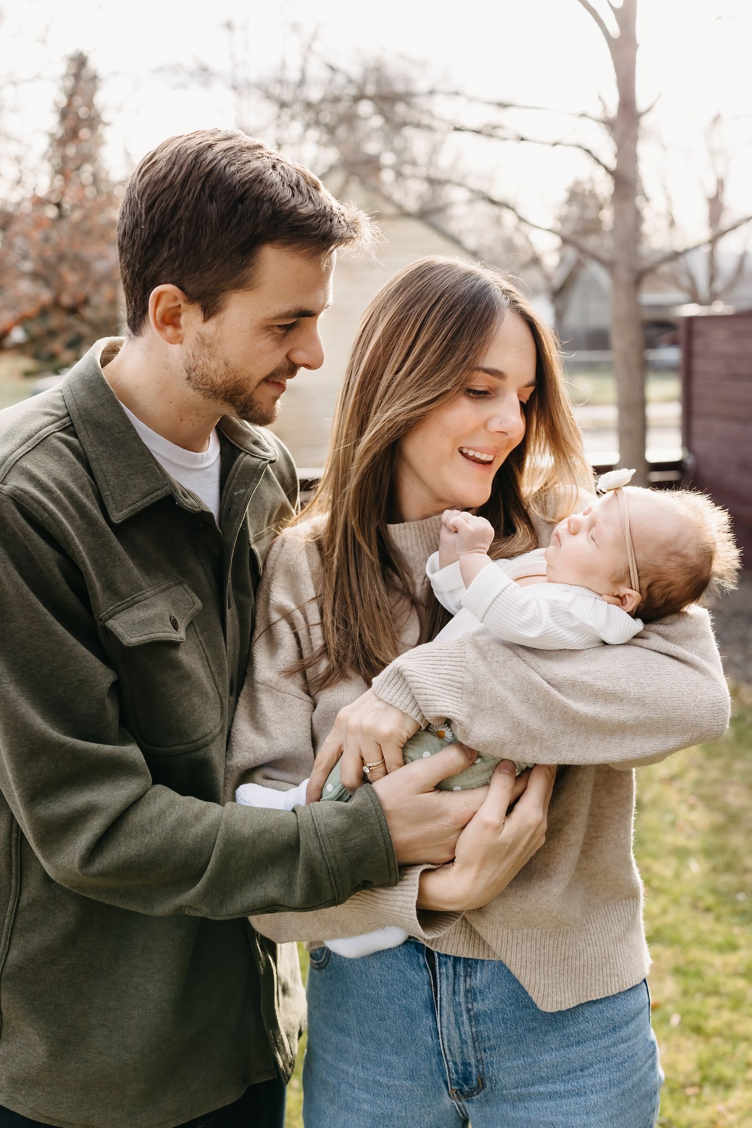 A couple in casual attire plays and laughs together with their baby outdoors on a fall day.