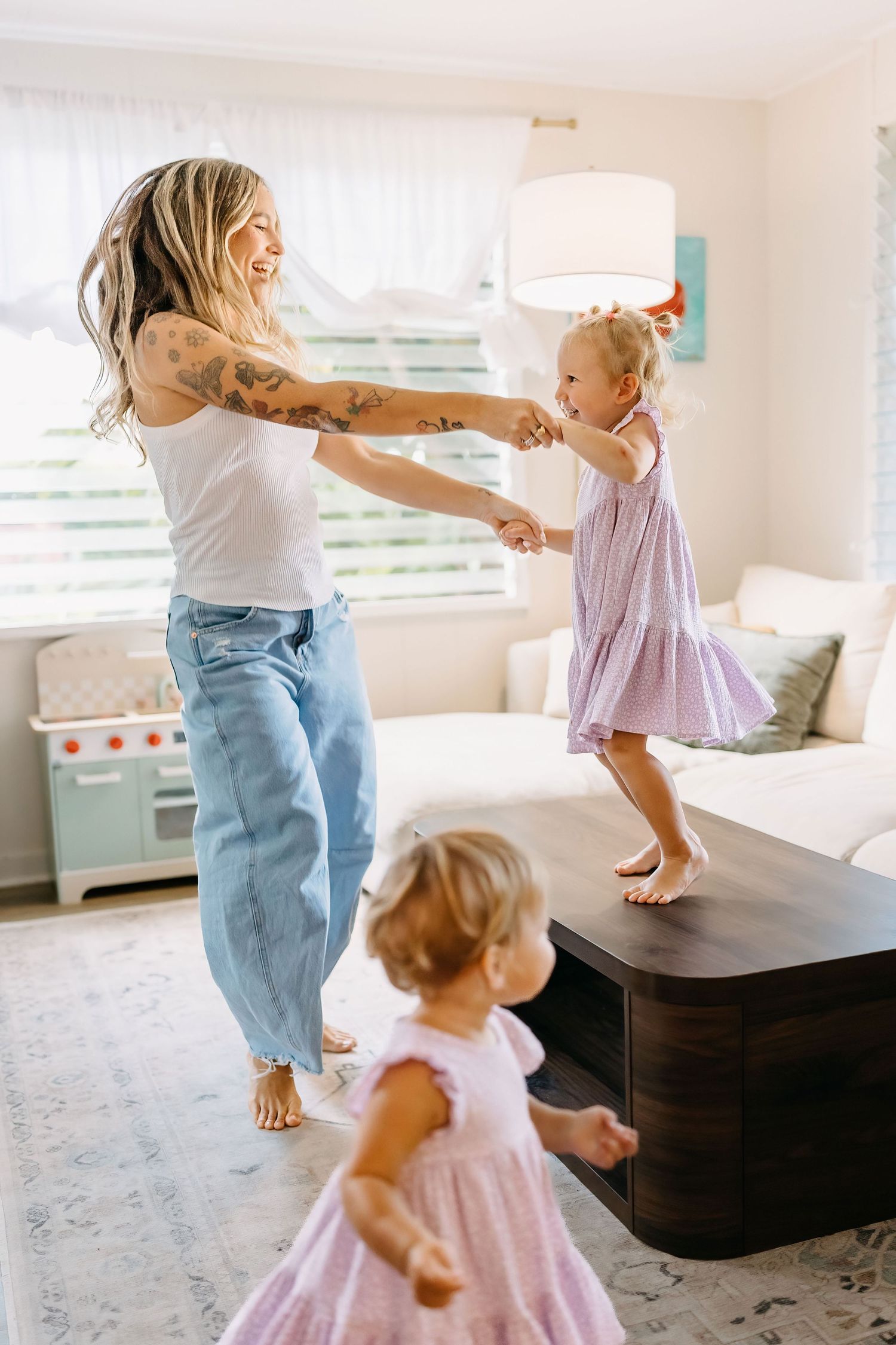 Parent and child dancing together barefoot on a light carpet in a bright white living room.