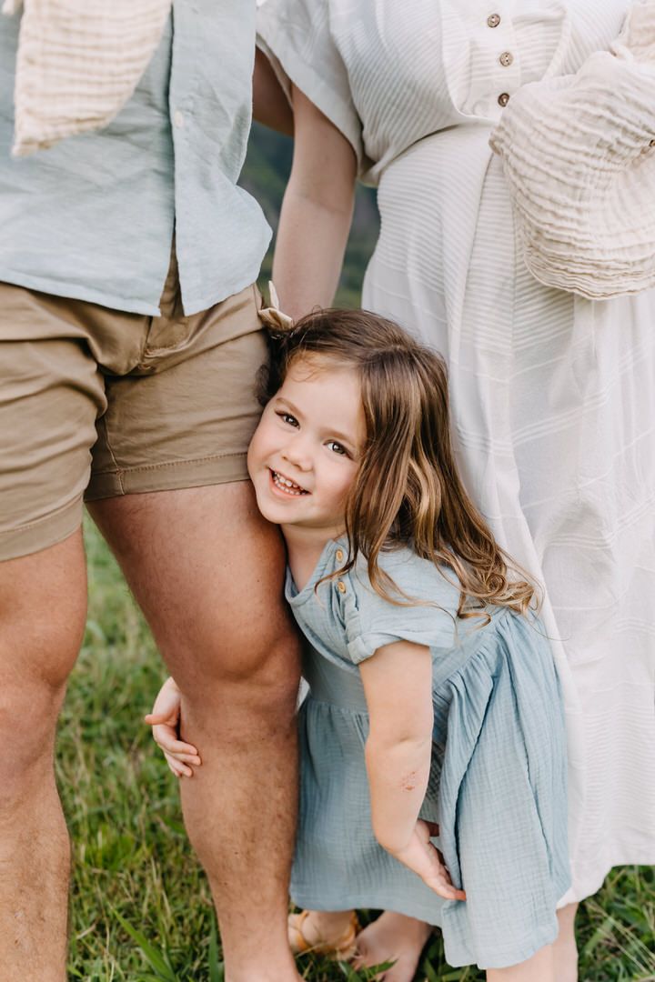 A playful sequence of a child in a blue dress peeking through legs in a grassy outdoor setting.