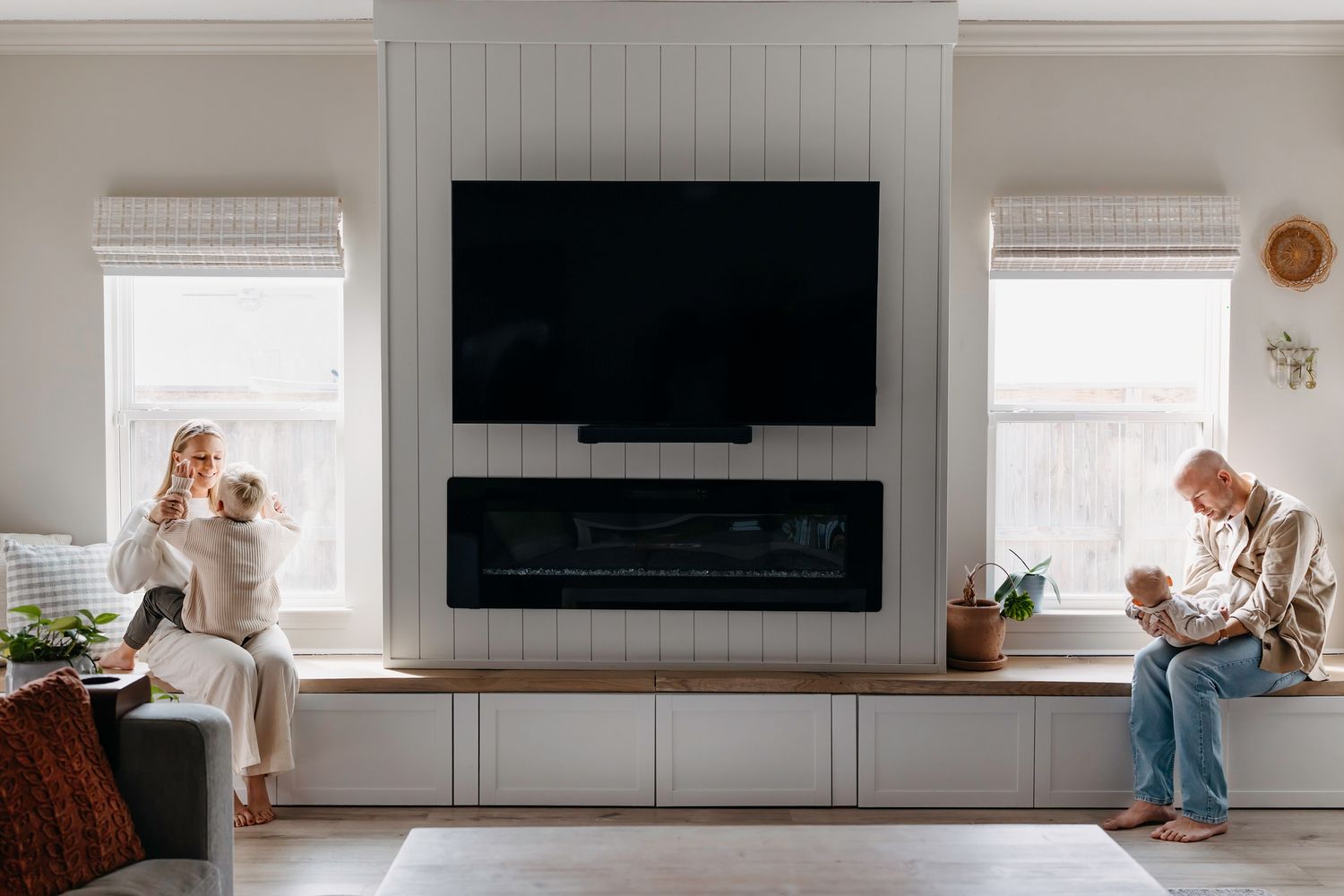 a wide photo of windows and a fireplace with mom and young son on one side and father and baby on the other side