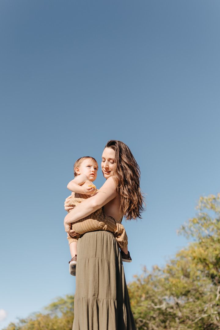 A tender moment captured outdoors as two people embrace against a bright blue sky and green foliage background.