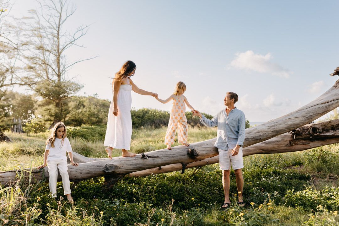 family in white outfits walk through a wildflower field at sunset while holding hands.