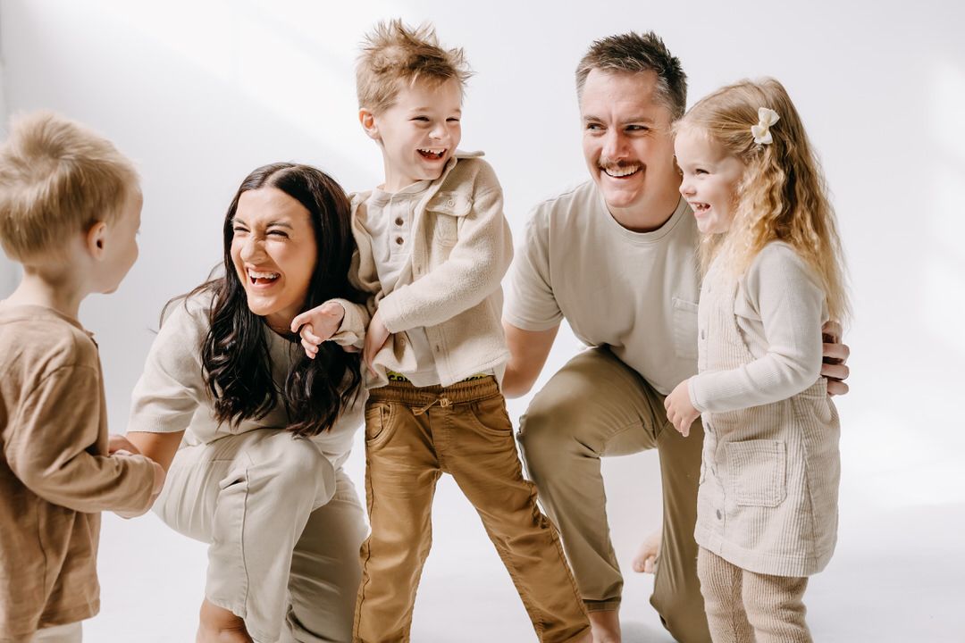Family members in neutral colored clothing share joyful moments together in a bright white studio setting.