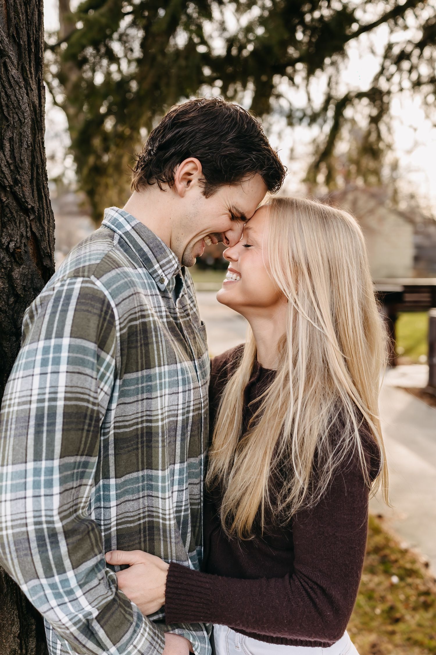 A couple embraces intimately in an outdoor setting with trees in the background during golden hour lighting.
