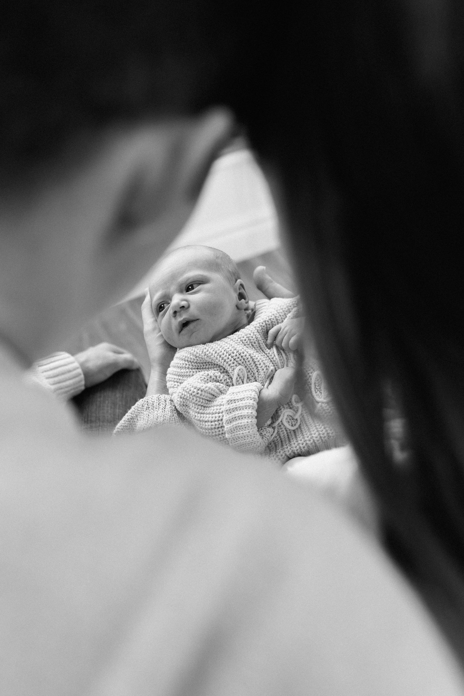 A black and white photo series showing a sleeping baby in soft knit clothing against white bedding.