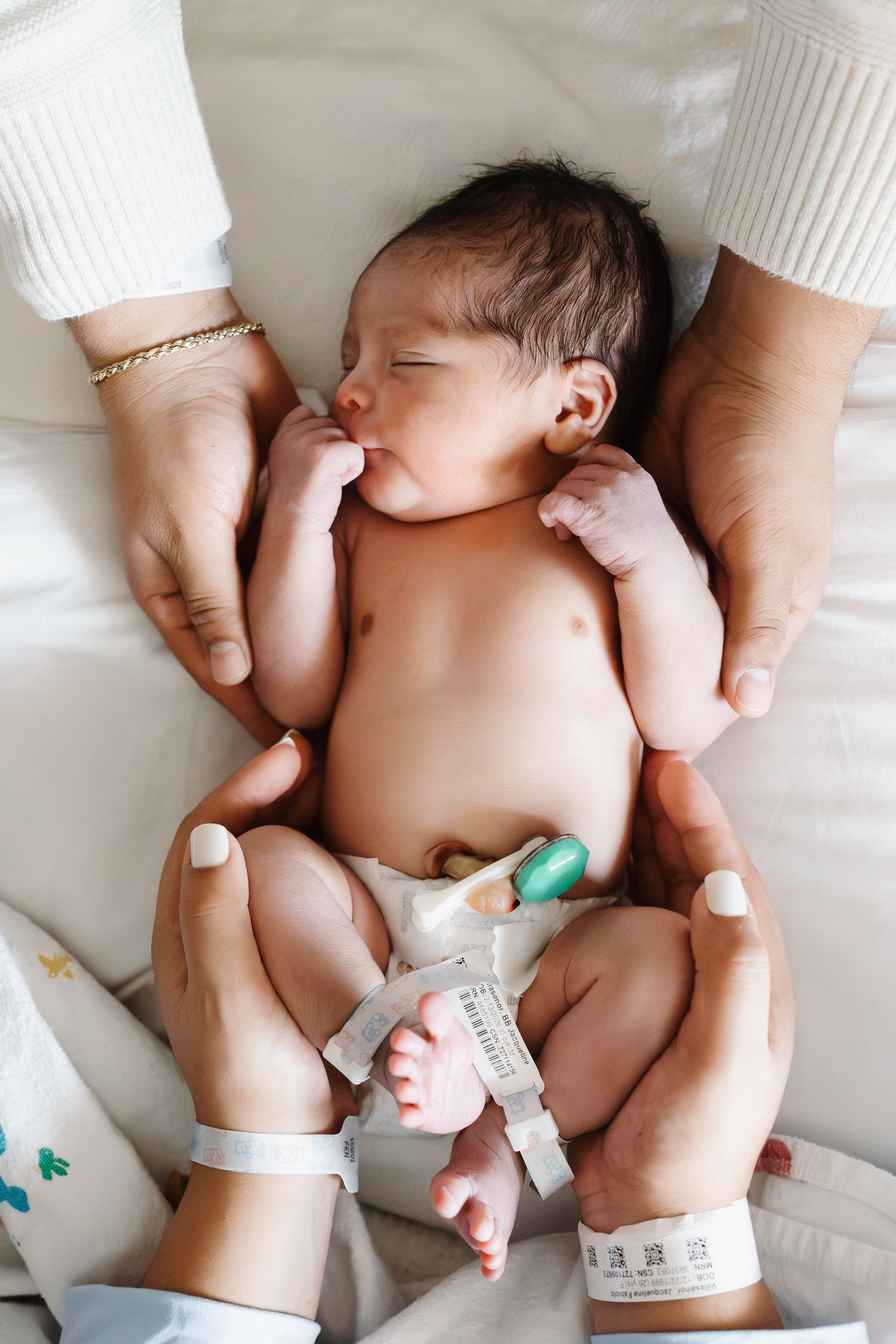 Newborn during fresh 48 photo session with mom and dads hands around him