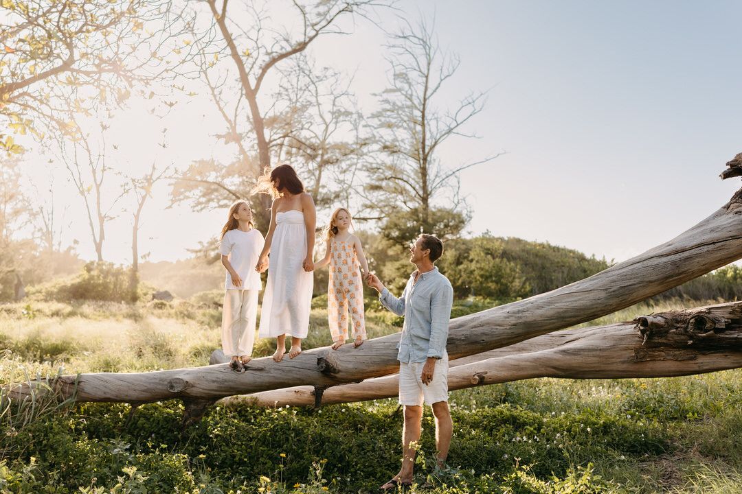 A group gathers on a fallen tree trunk at sunset in a grassy field during a casual outdoor photoshoot.