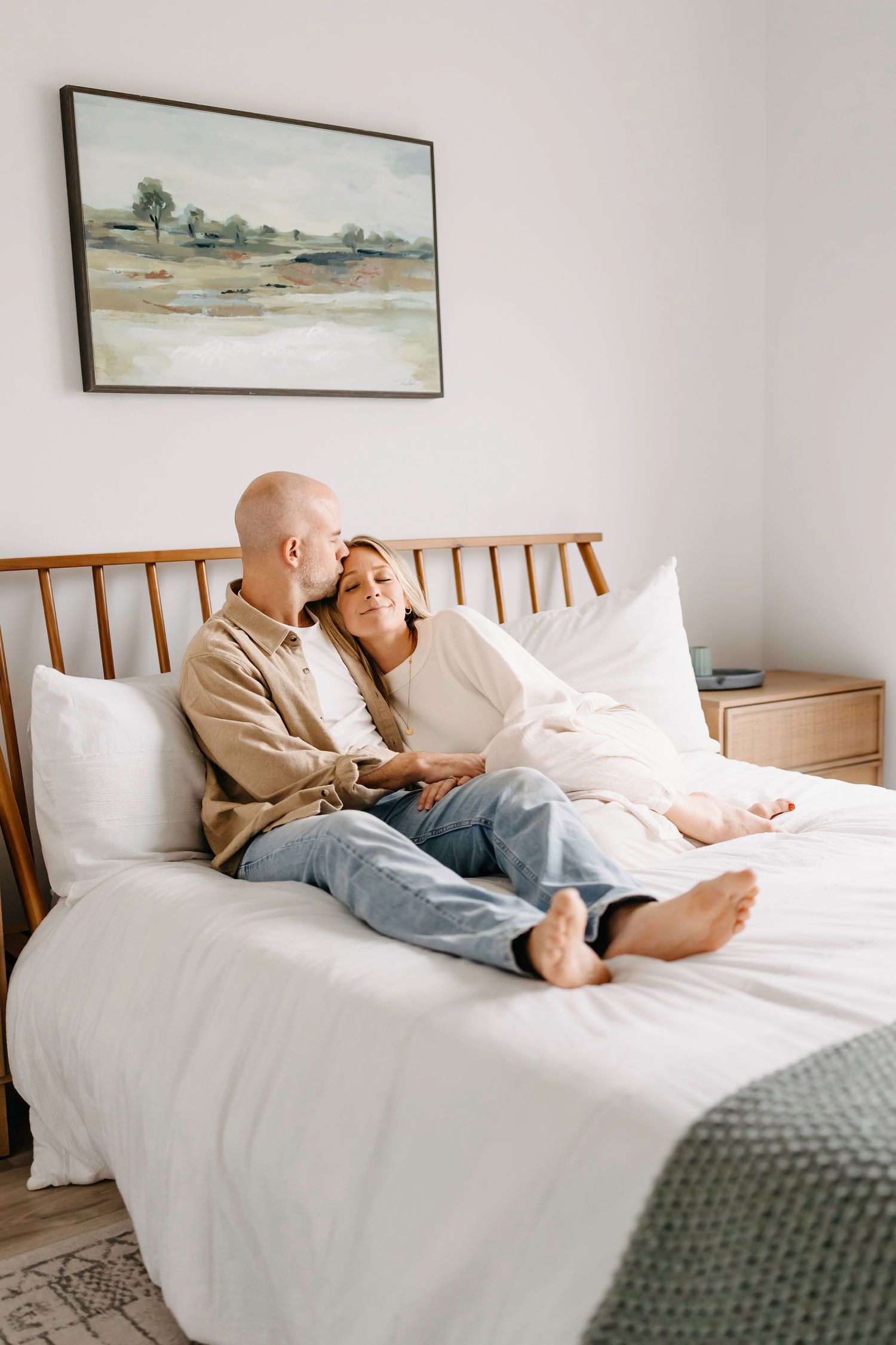 Two people lying on a white bed with artwork on the wall in a minimalist bedroom interior.